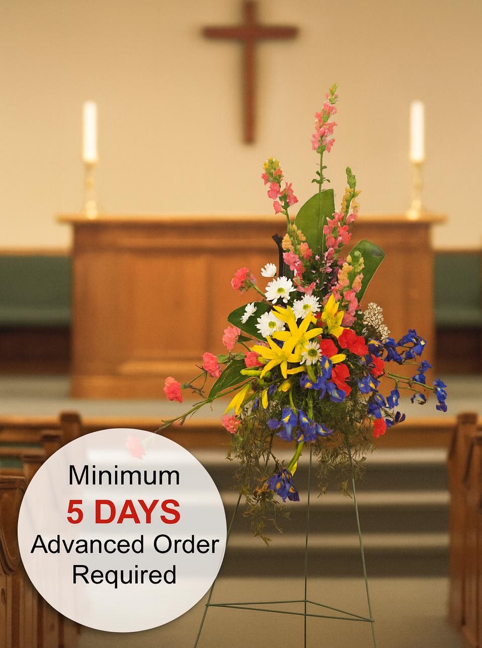 Tall multicolored standing spray with yellow lilies and mixed flowers on an easel in a church.