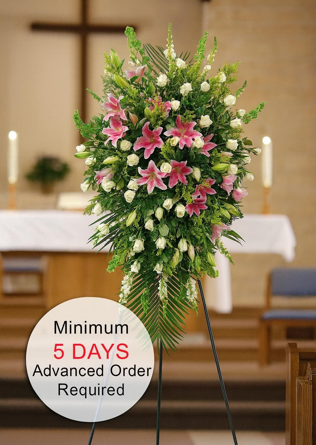 Tall standing spray with pink lilies and white roses on a metal easel in a church.