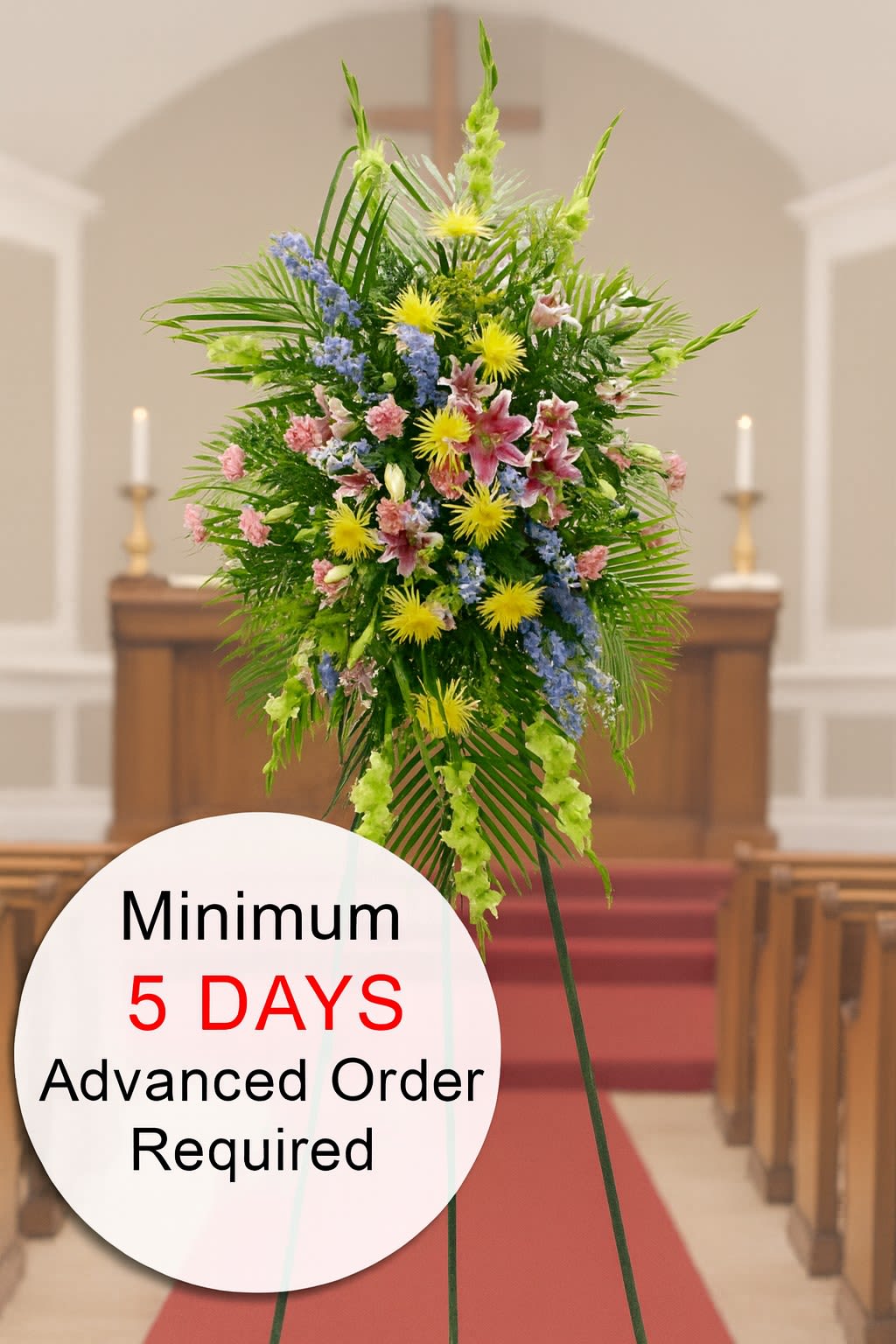 Tall standing funeral spray of pink, yellow, and blue flowers on an easel in a church aisle