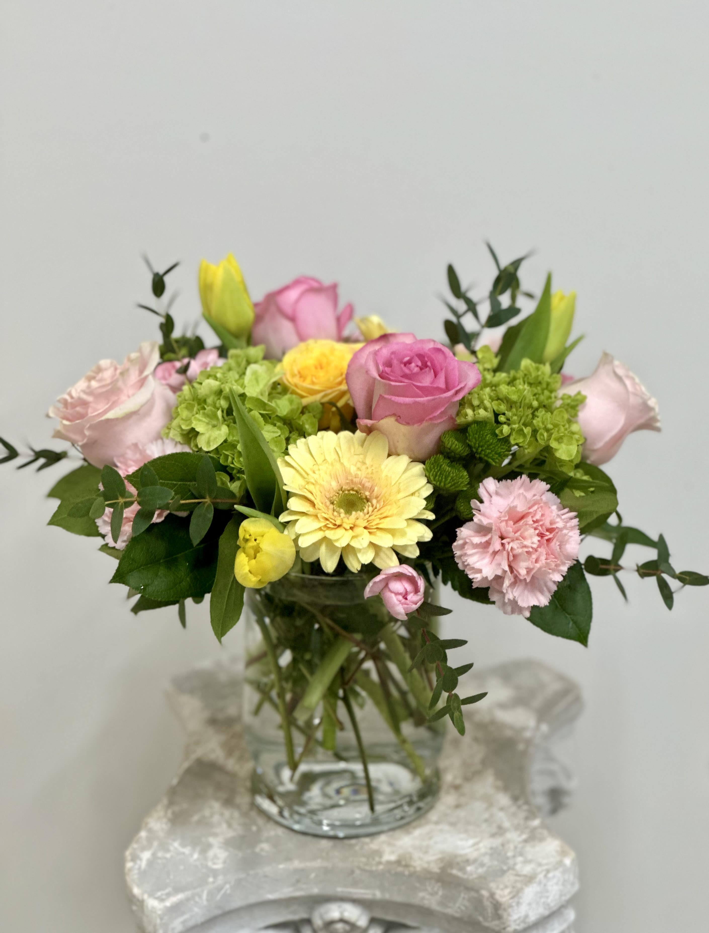 Mixed pink and yellow flowers arranged in a glass vase