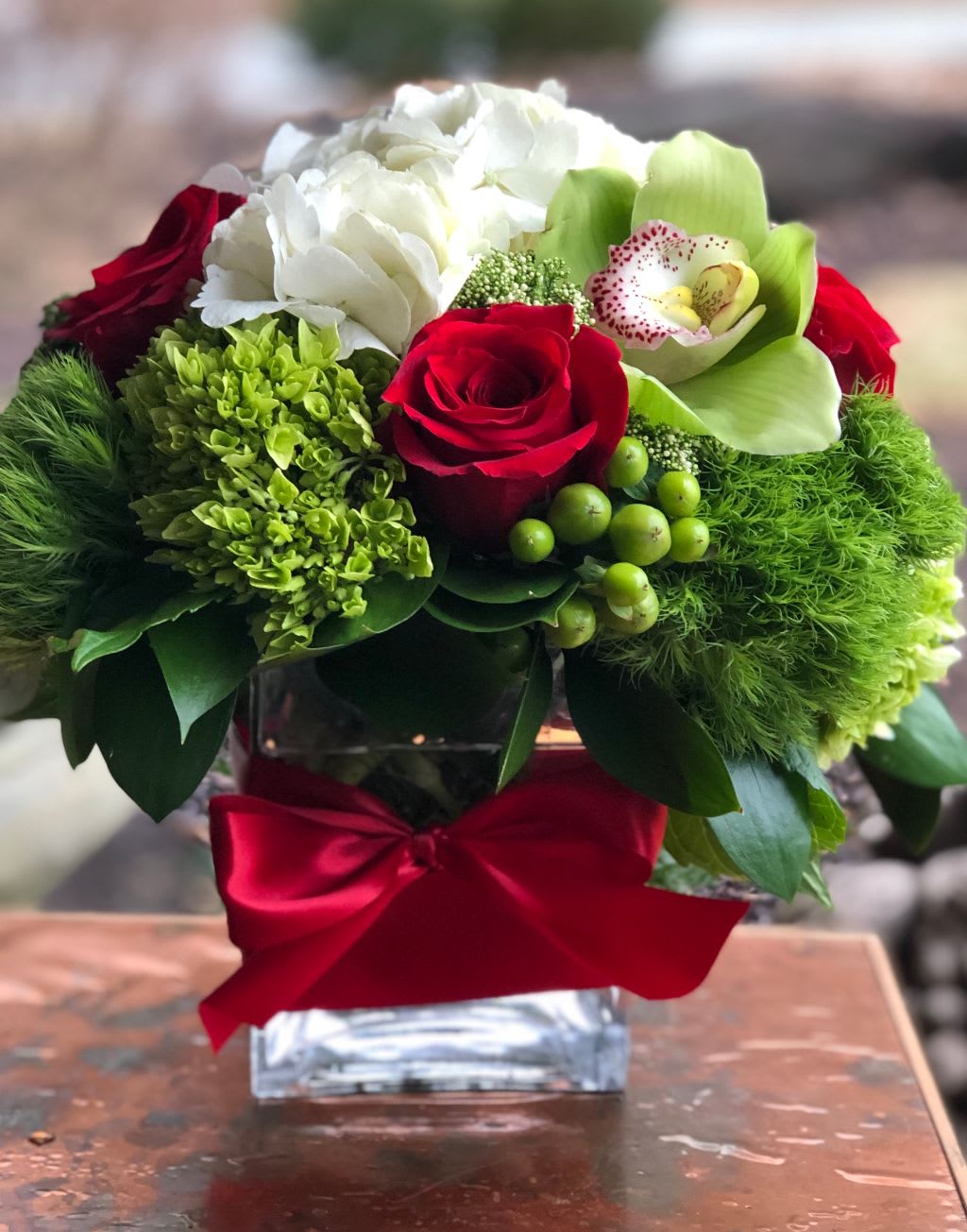 Red roses and white blooms in a glass vase with a red ribbon