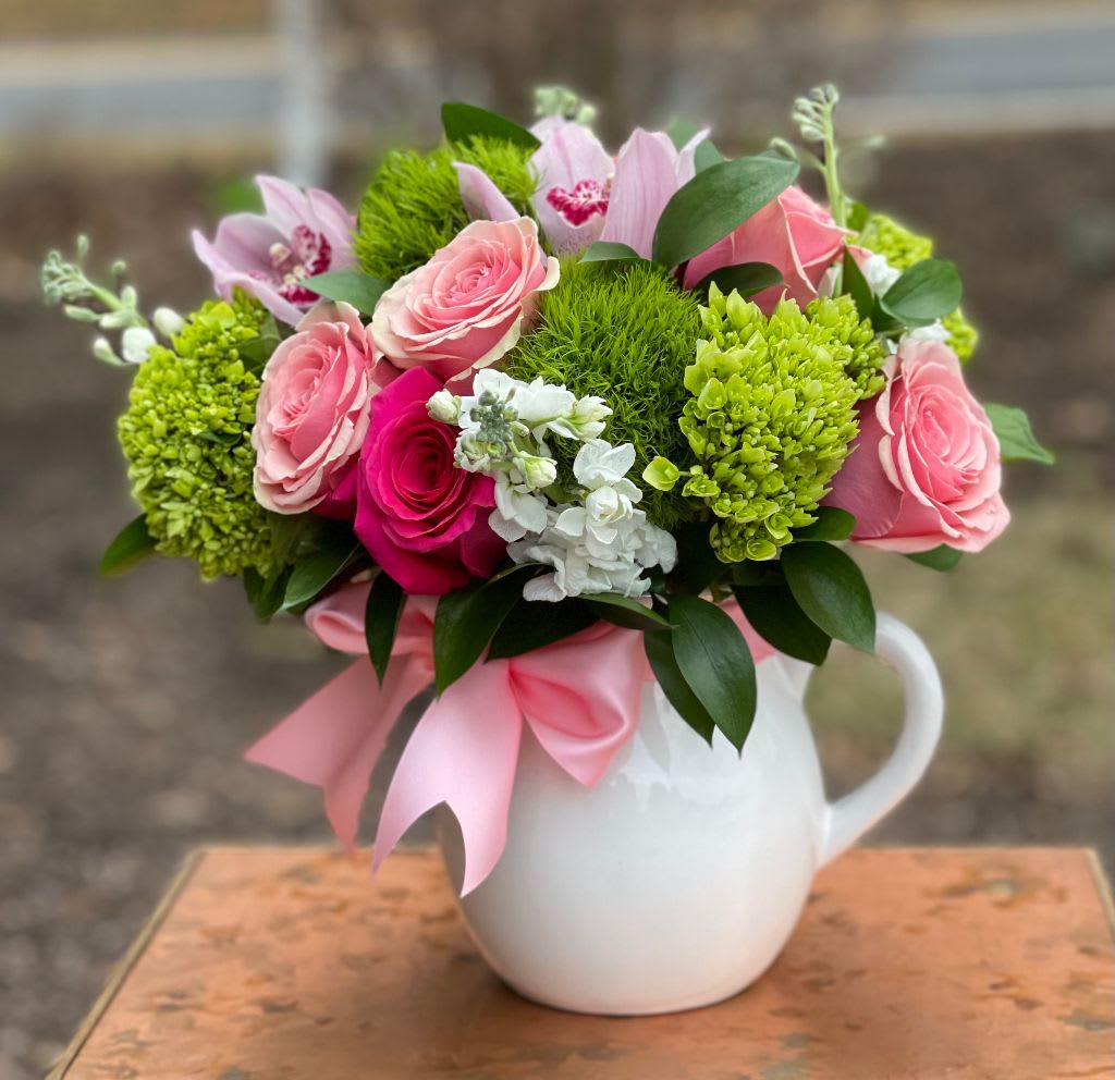 Pink roses and green blooms arranged in a white pitcher vase
