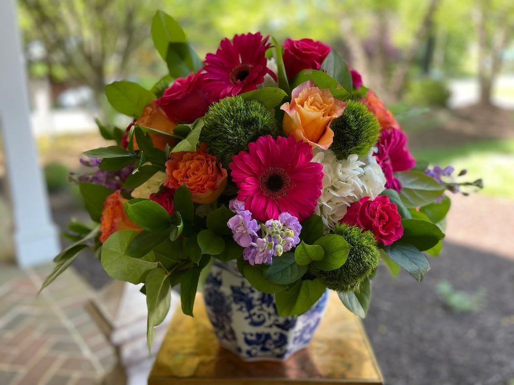 Grace and Elegance - Grace and Elegance – Vibrant Mixed Floral Arrangement | Wilmington, Delaware Local Florist  Make a lasting impression with Grace and Elegance, a luxurious floral arrangement designed by your trusted Wilmington, Delaware florist. This vibrant bouquet features rich dark pink roses, bright orange roses, crisp white hydrangea, textured green trichilium, bold dark pink Gerber daisies, and fragrant lavender stock. Artfully arranged in a stylish blue and white container, this design brings color, beauty, and sophistication to any space.  Perfect for birthdays, anniversaries, celebrations, or just because. Available for same-day flower delivery in Wilmington, DE and surrounding areas. Choose our local flower shop for premium, fresh blooms and exceptional service.