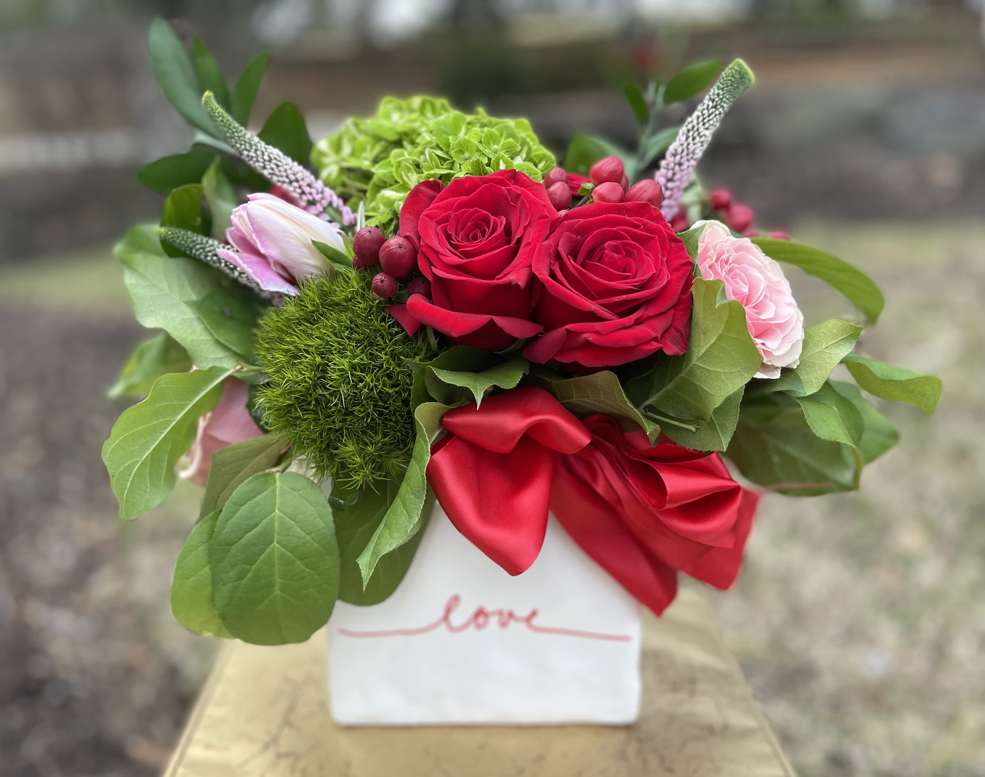 Red roses and pink blooms in a white vase with a red ribbon