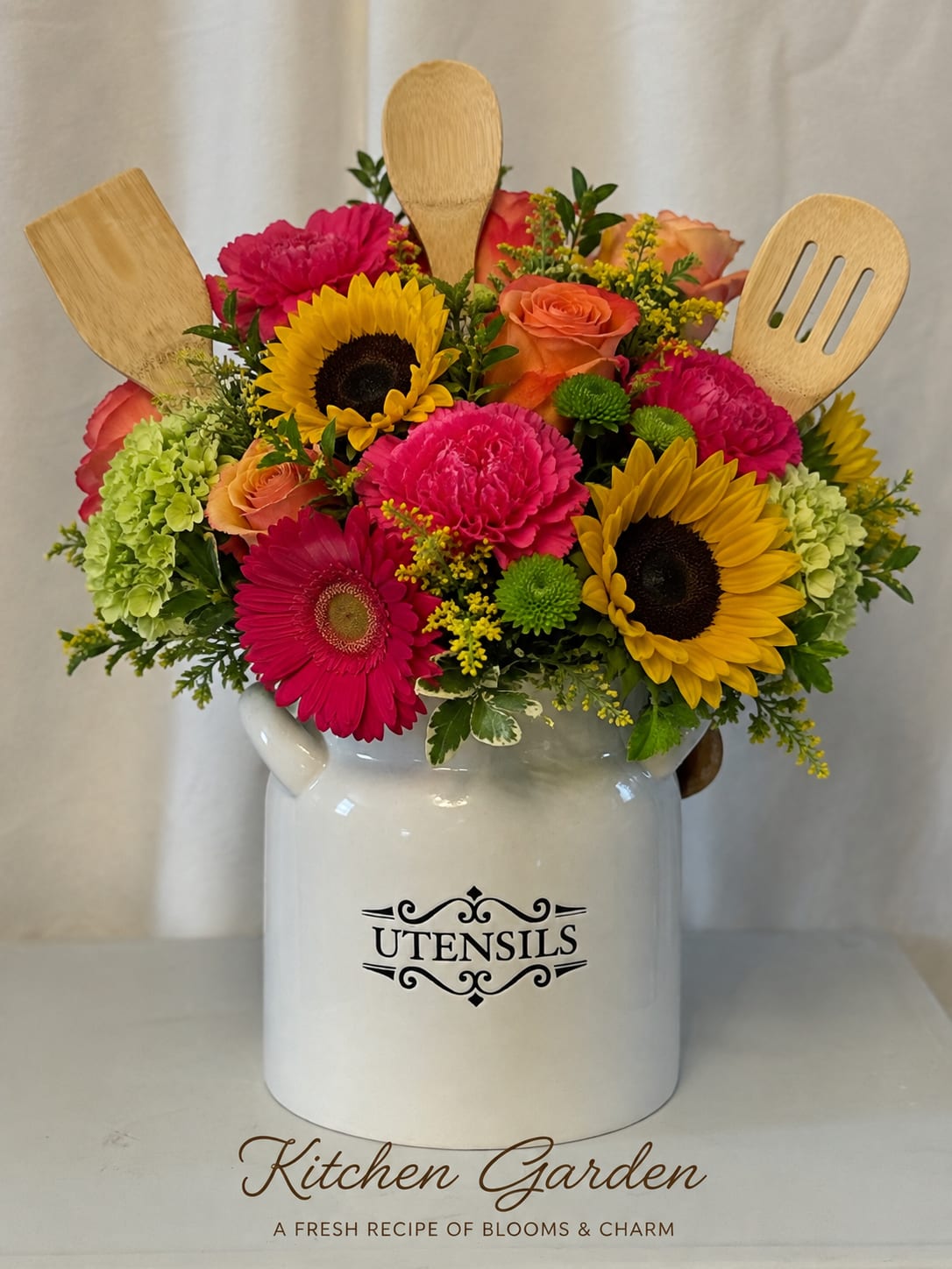 Bright mixed flower arrangement in a white utensil jar with wooden kitchen tools