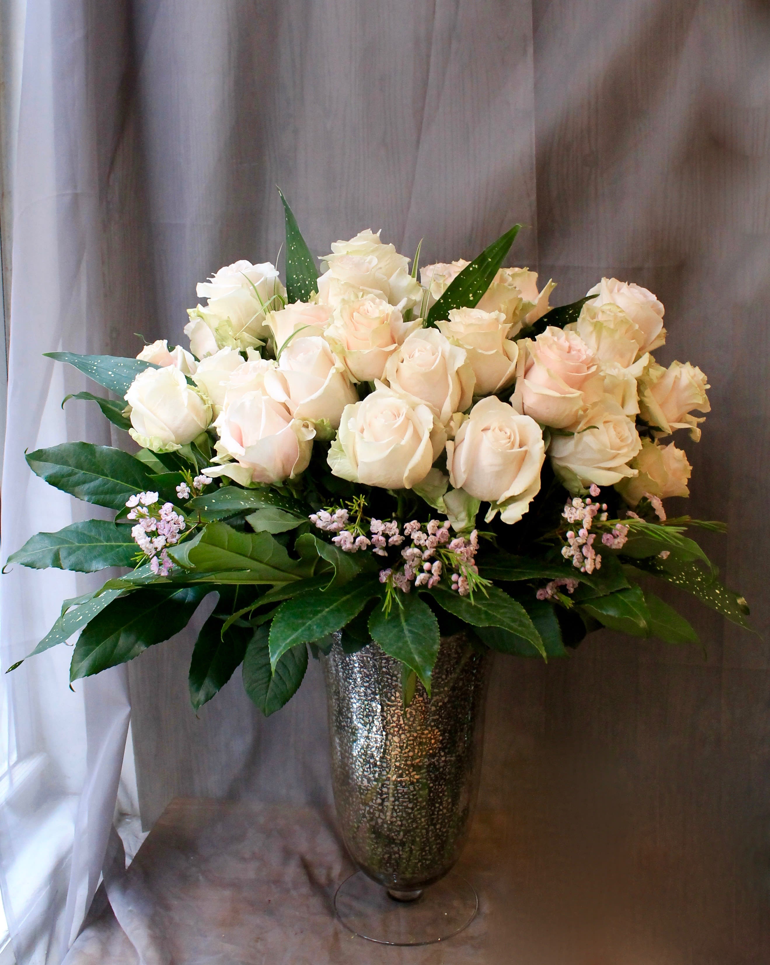 Cream rose arrangement in a tall silver vase