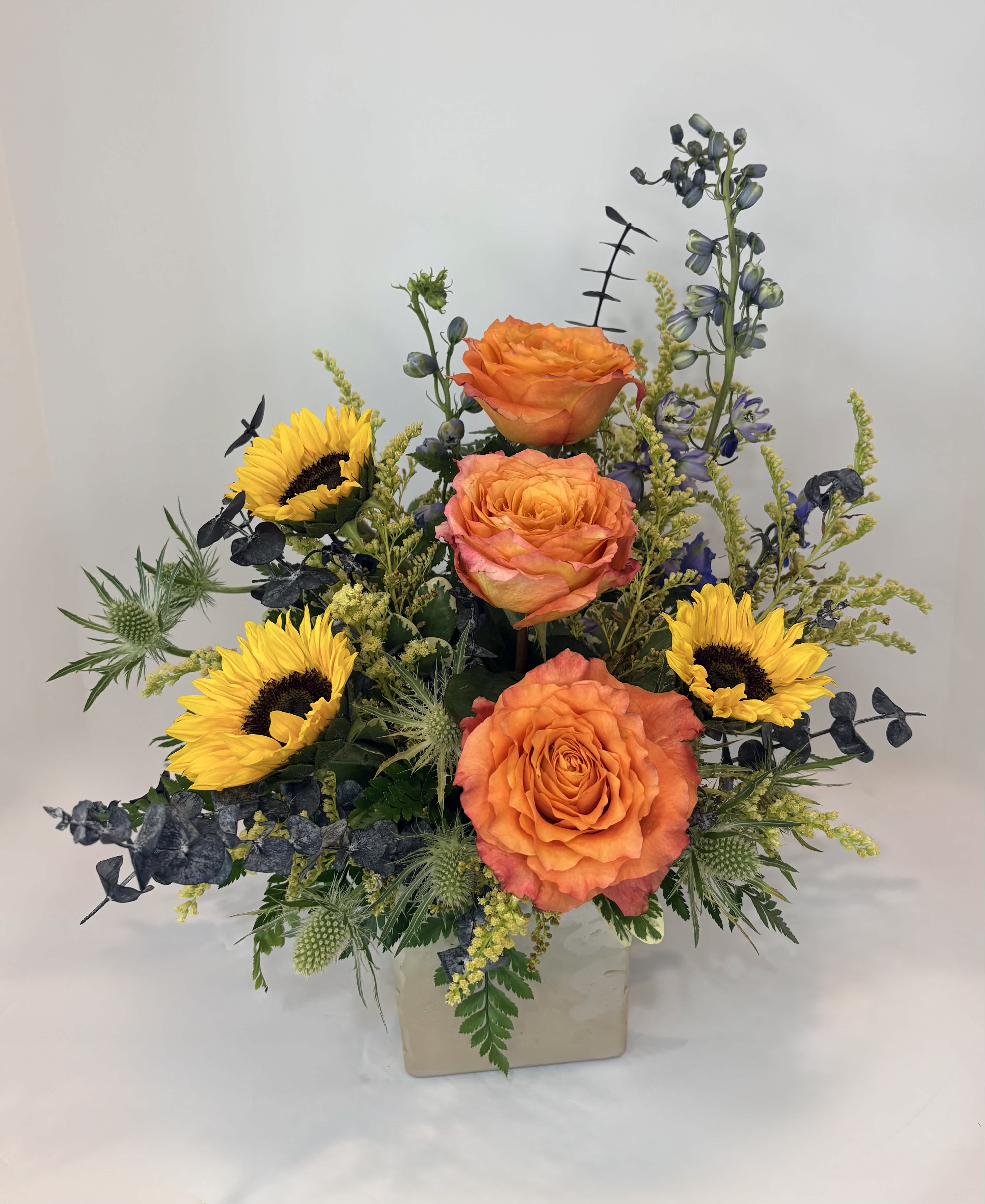 Orange roses and yellow sunflowers in a square vase