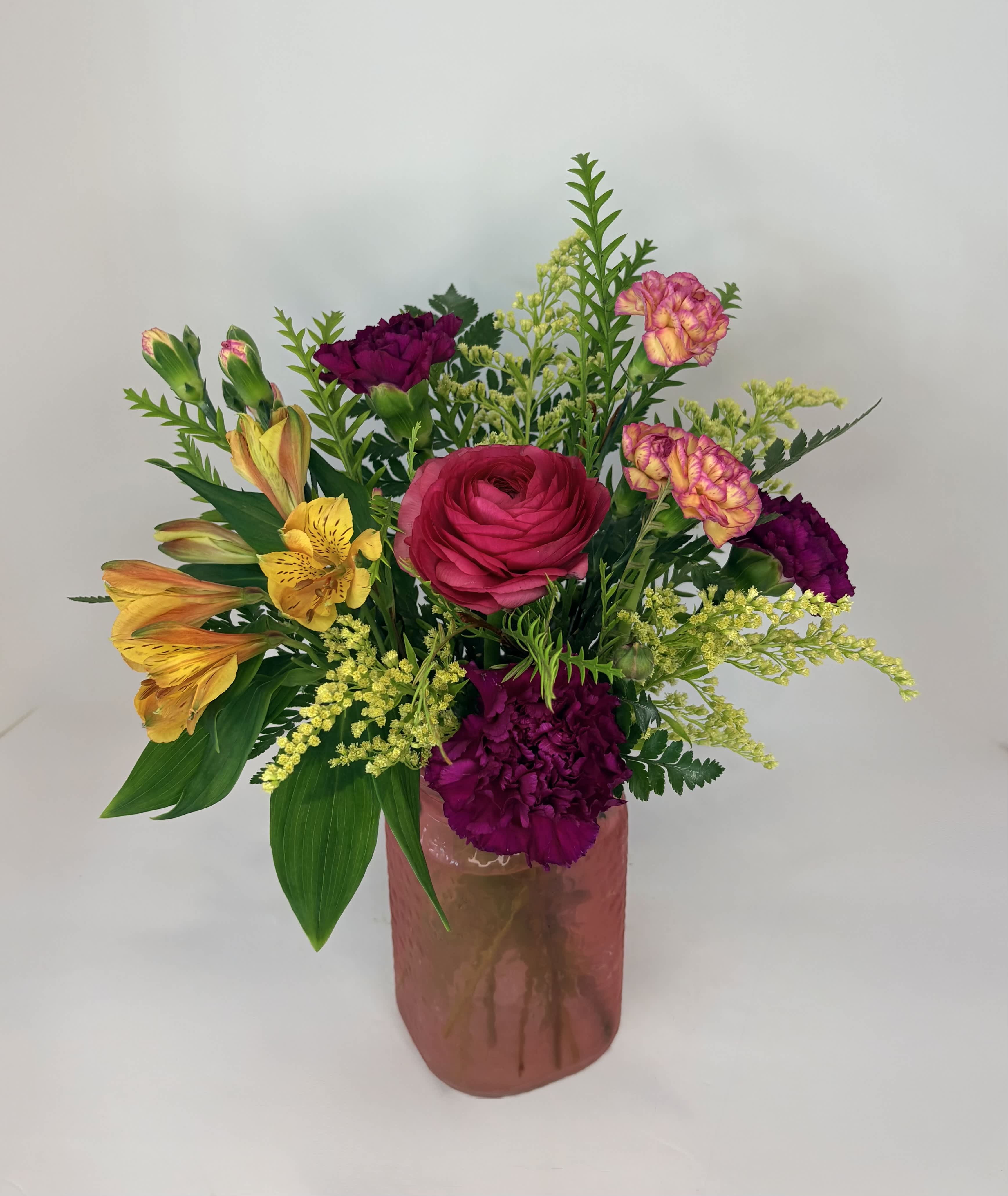 Mixed bouquet in a pink glass vase with bright pink, yellow, and purple flowers