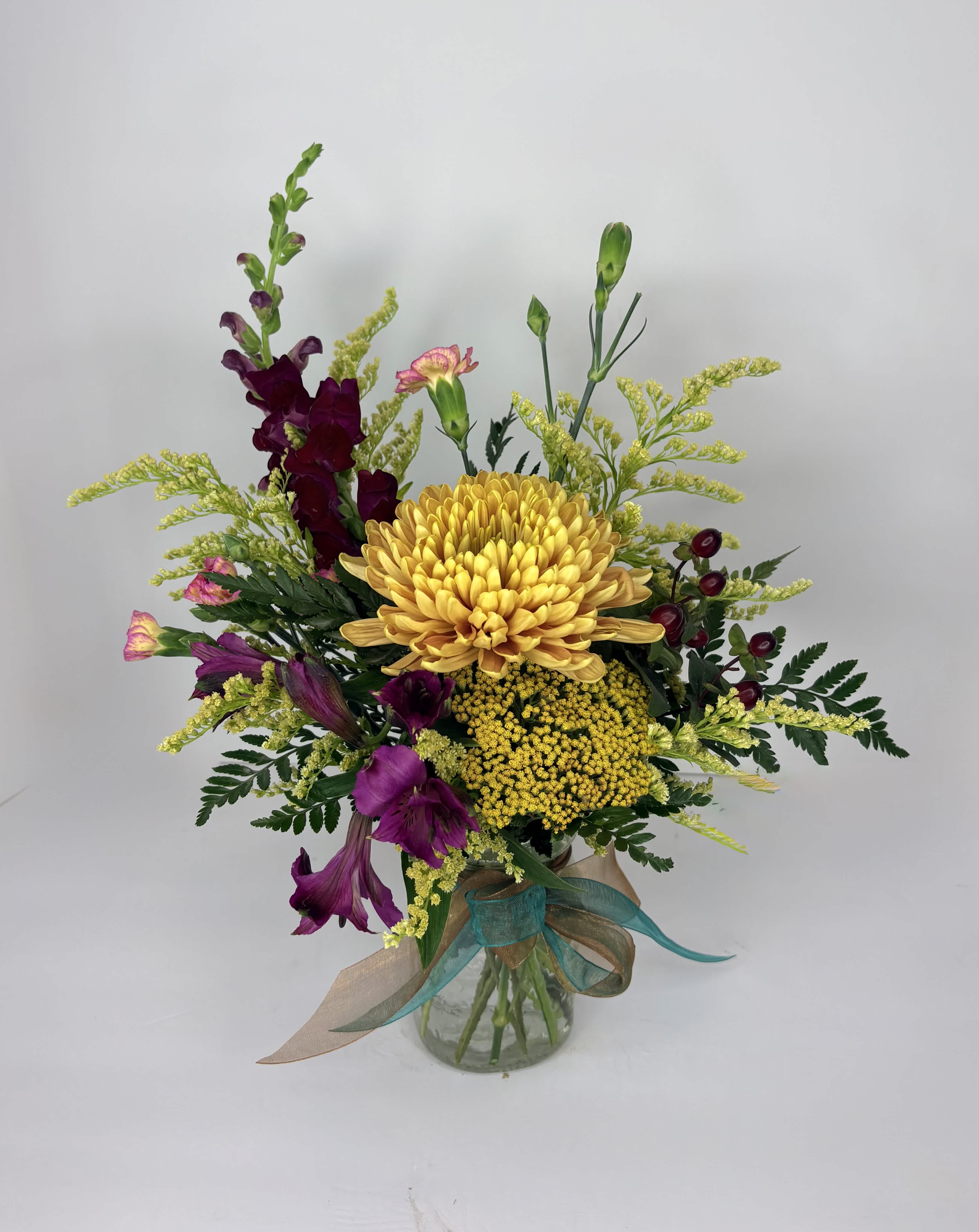 Mixed bouquet of yellow and purple flowers in a glass vase with ribbon