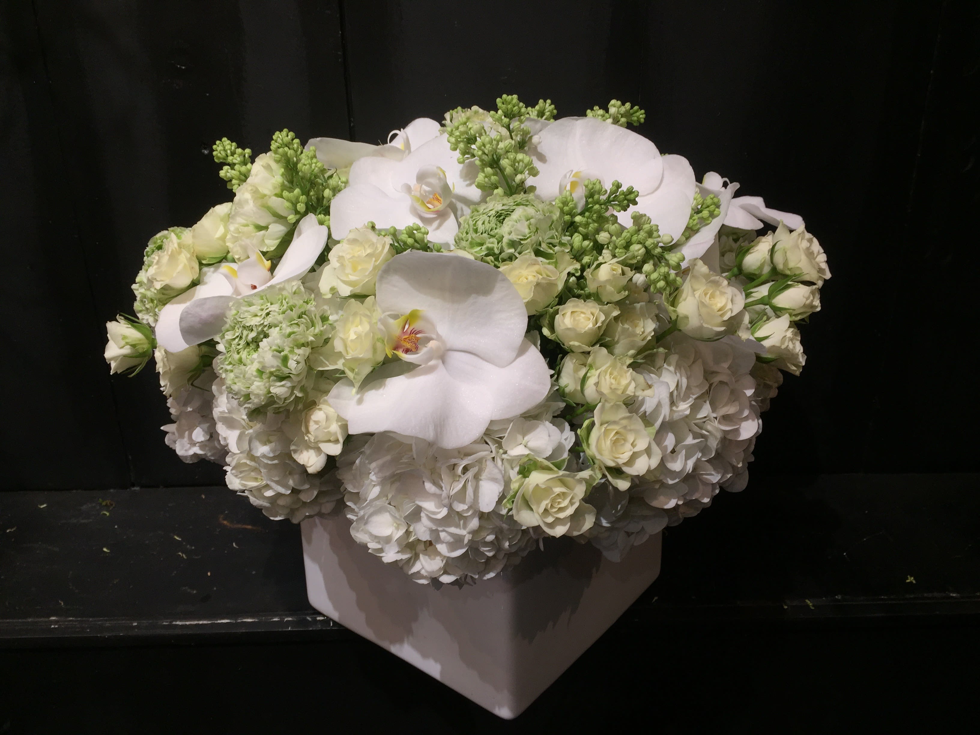 White floral arrangement in a square vase with orchids and roses