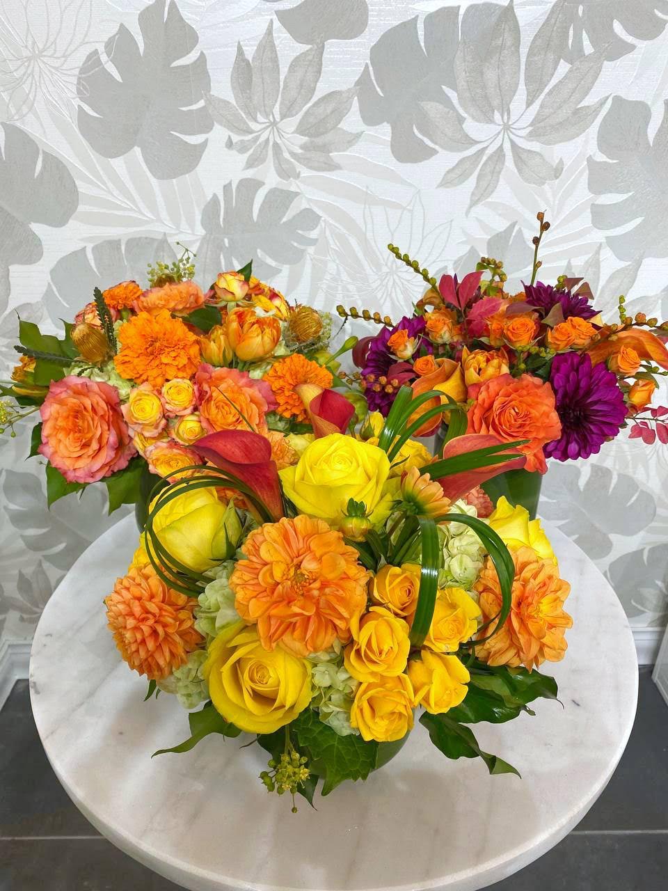 Three colorful floral arrangements with roses and dahlias on a round table