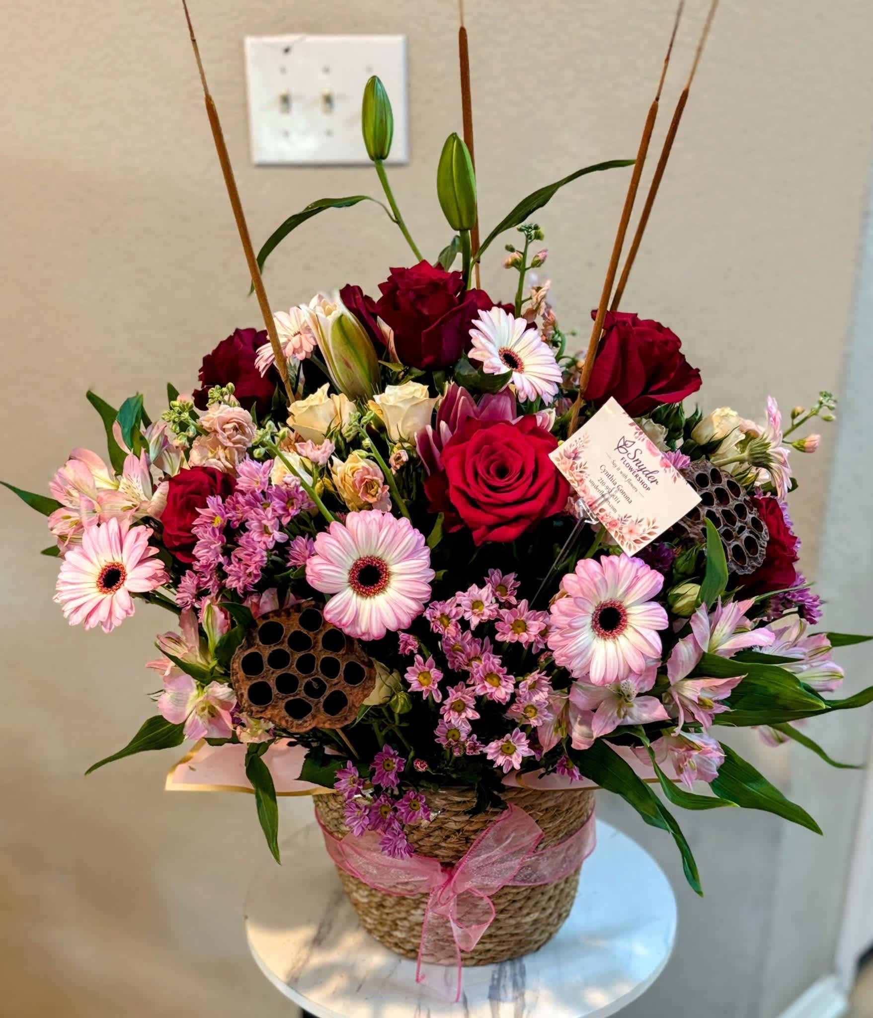 Mixed pink and red flower arrangement in a woven basket with a ribbon