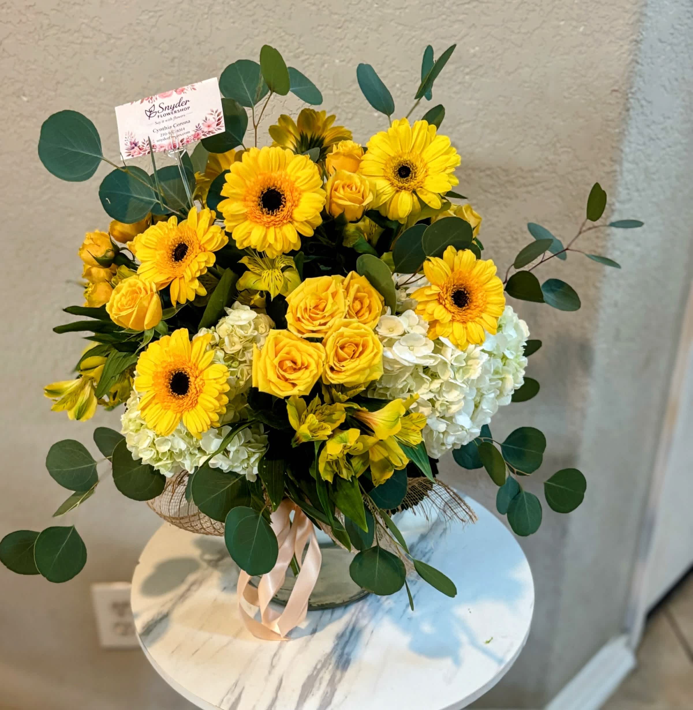 Yellow gerbera daisies and roses in a glass vase with greenery