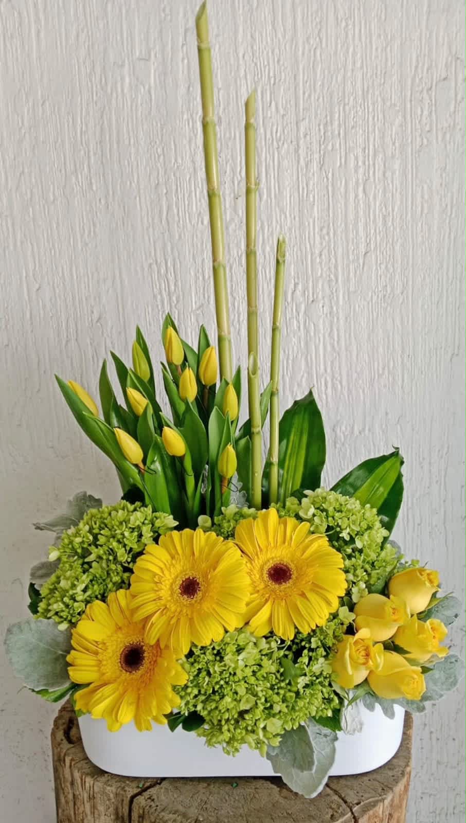 Yellow gerberas and tulips arranged with bamboo in a white container