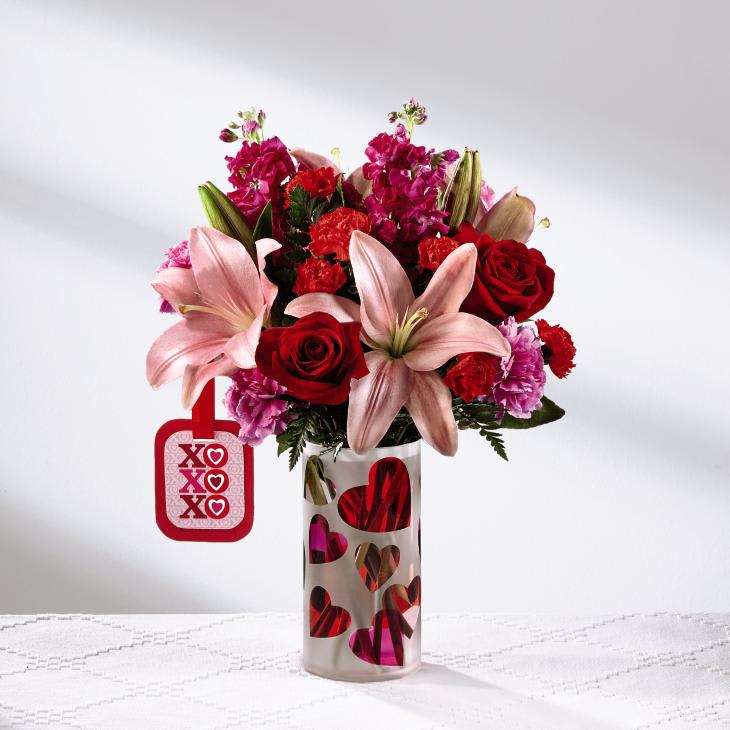 The FTD Love You XO Bouquet by Hallmark - Love is in the air this Valentine's Day! The FTDÂ¨ Love You XOÂª Bouquet by Hallmark is the perfect way to celebrate the loves in your life, whether it be your sweetheart, a favorite family member, or your best friend. Pink Asiatic Lilies capture their attention with their large star-shaped blooms set against a blushing backdrop of red roses, red mini carnations, hot pink carnations, hot pink gilly flower and lush greens. Arranged with a loving hand within a keepsake frosted glass vase with a pink and red heart design throughout, this Valentine flower bouquet is presented with a Hallmark tag that reads, "Love You!" on one side and, "XO, XO, XO," on the other to create a beautiful way to celebrate love this coming February 14th. GOOD bouquet includes 9 stems. Approx. 14"H x 12"W. BETTER bouquet includes 12 stems. Approx. 16"H x 13"W. BEST bouquet includes 15 stems. Approx. 17"H x 14"W. EXQUISITE bouquet includes 20 stems. Approx. 18"H x 15"W.