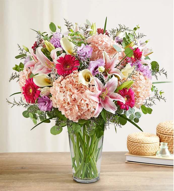 Mixed bouquet of pink lilies, hydrangeas, gerbera daisies, and calla lilies in a glass vase
