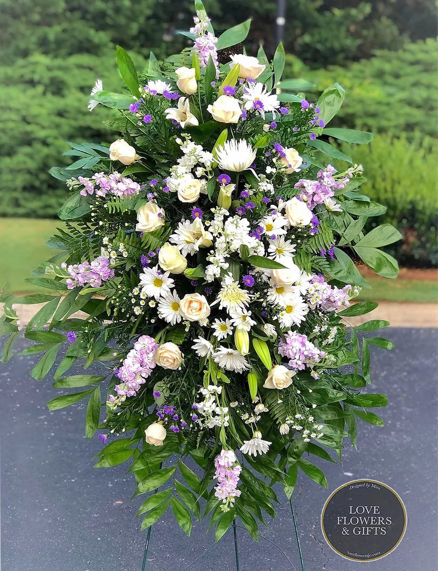 Tall standing spray of white and cream flowers with purple accents on an easel stand