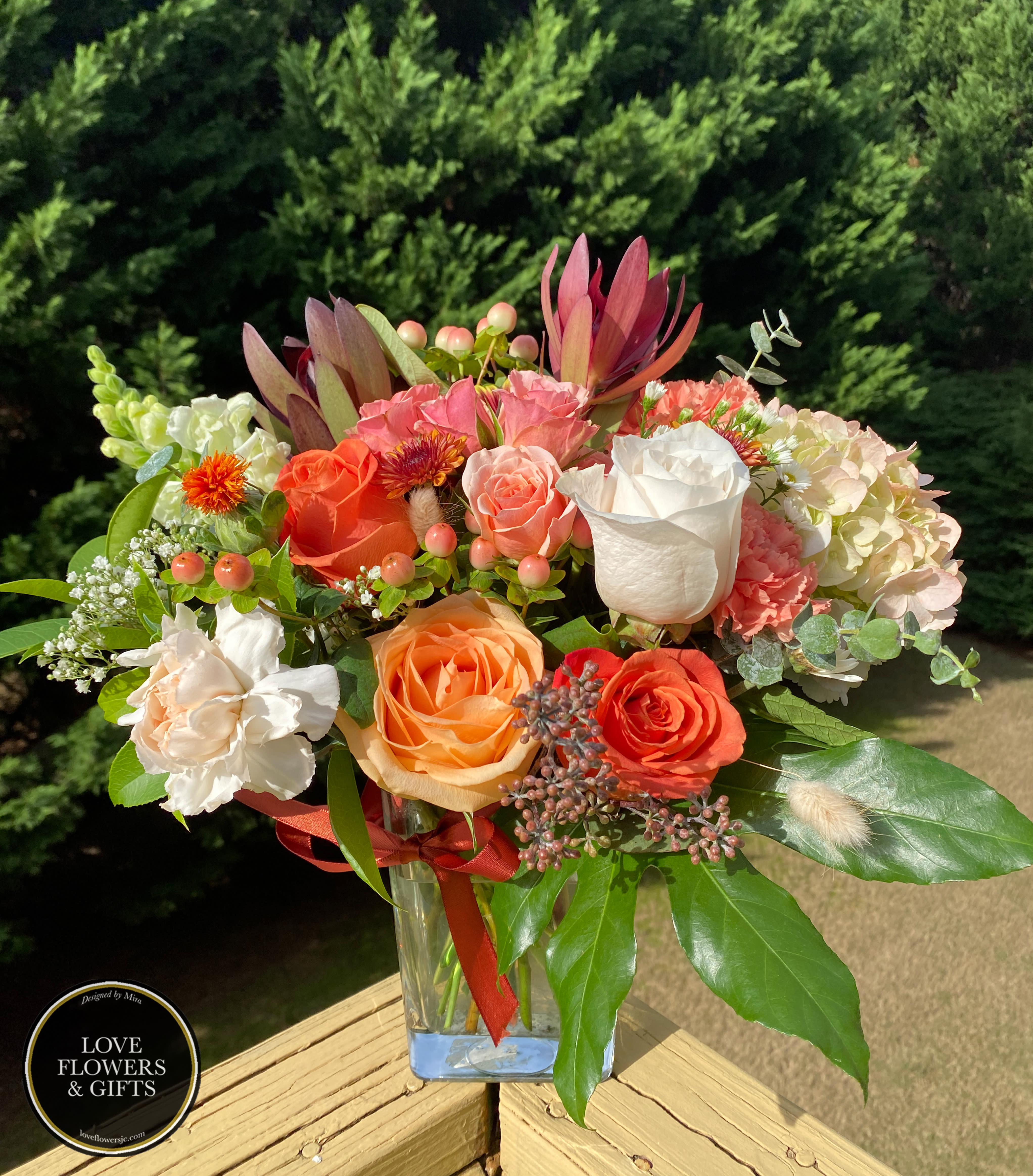 Mixed bouquet of orange, peach, and white flowers in a clear glass vase on a wooden railing
