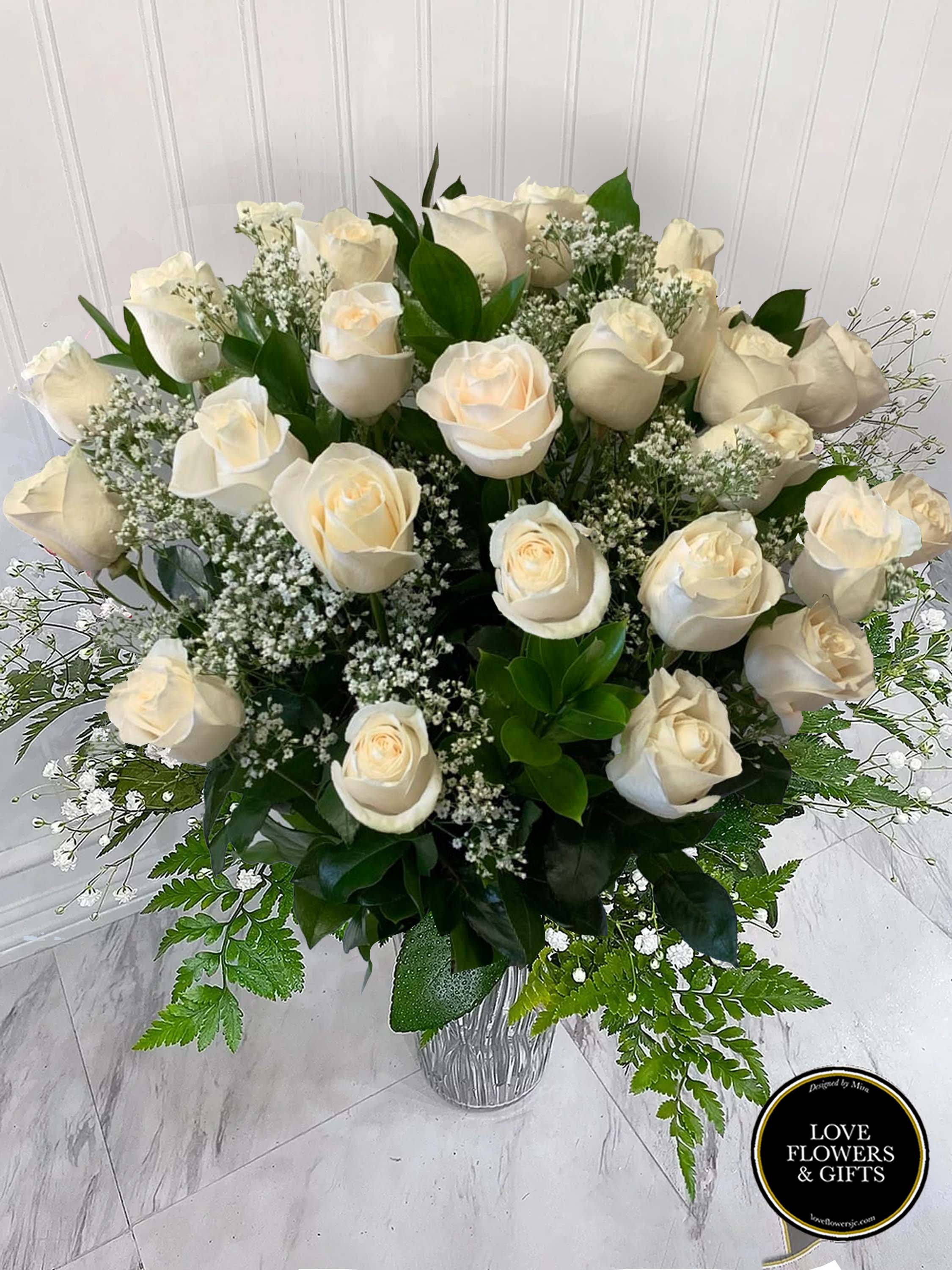 Tall arrangement of white roses and baby’s breath in a clear glass vase
