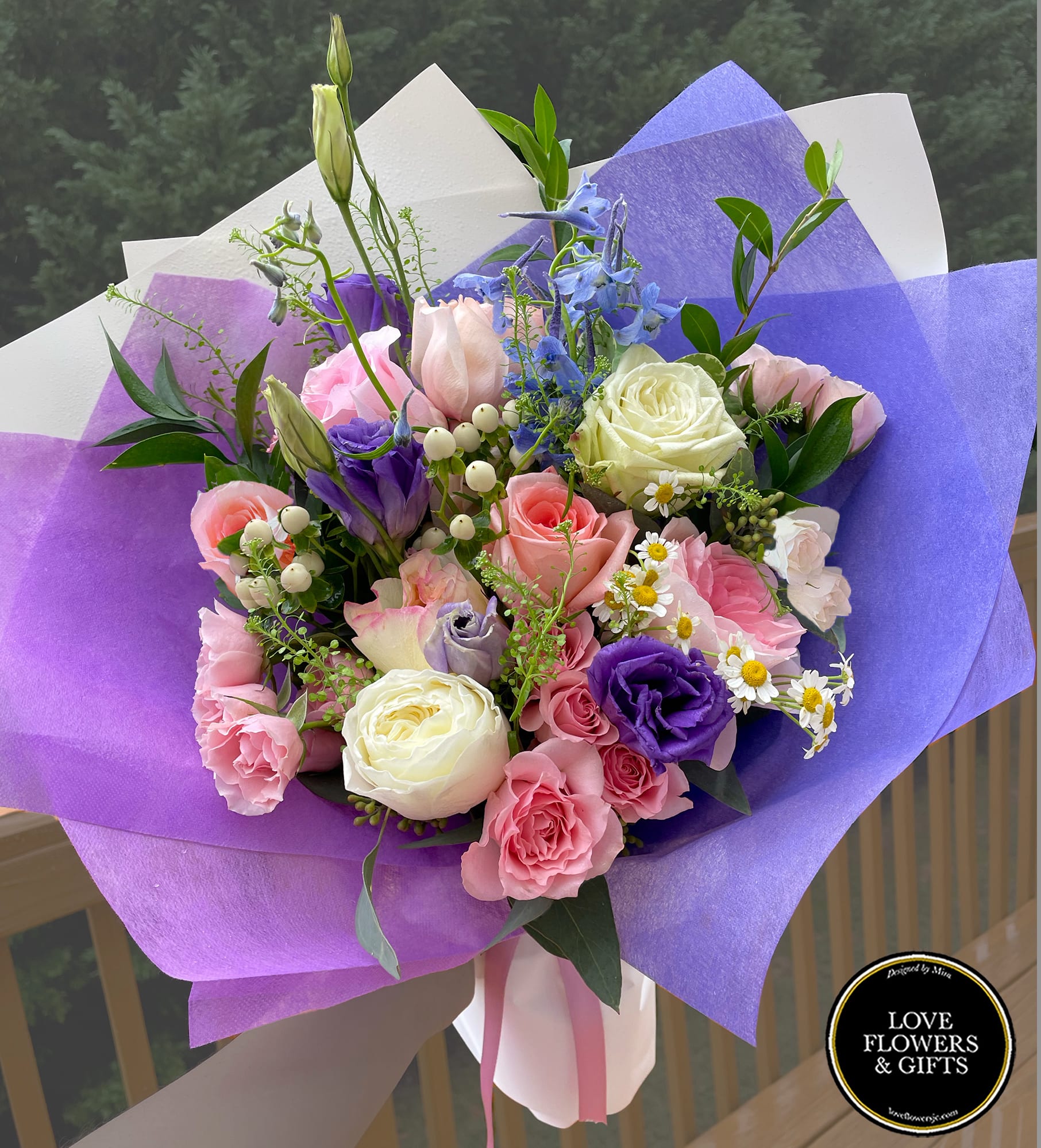 Hand-tied bouquet of pink roses, purple lisianthus, and white blooms wrapped in purple and white paper