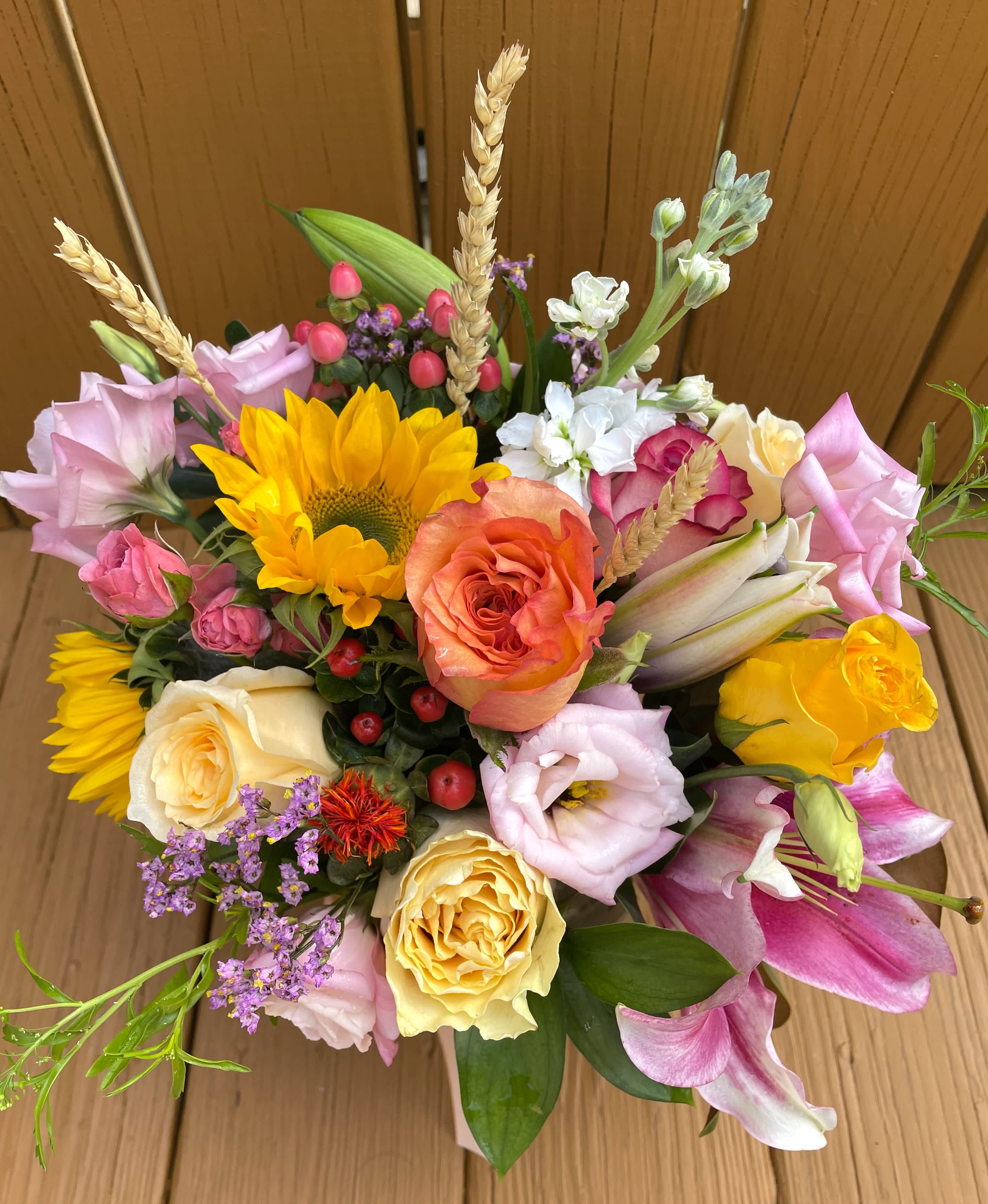Vibrant mixed bouquet with sunflowers, roses, lilies, and lisianthus in a low container