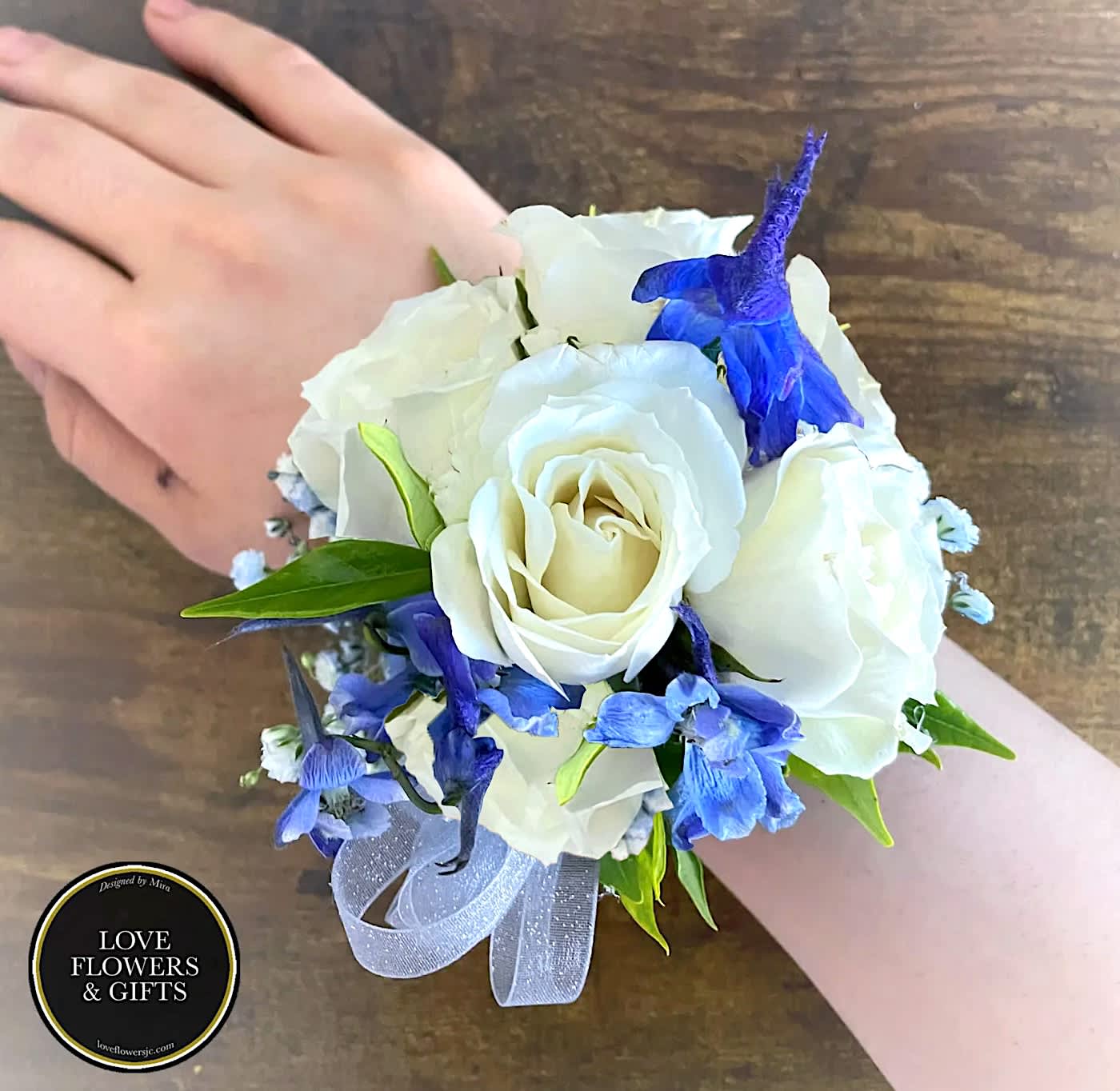 White rose and blue flower wrist corsage with ribbon on a person’s wrist