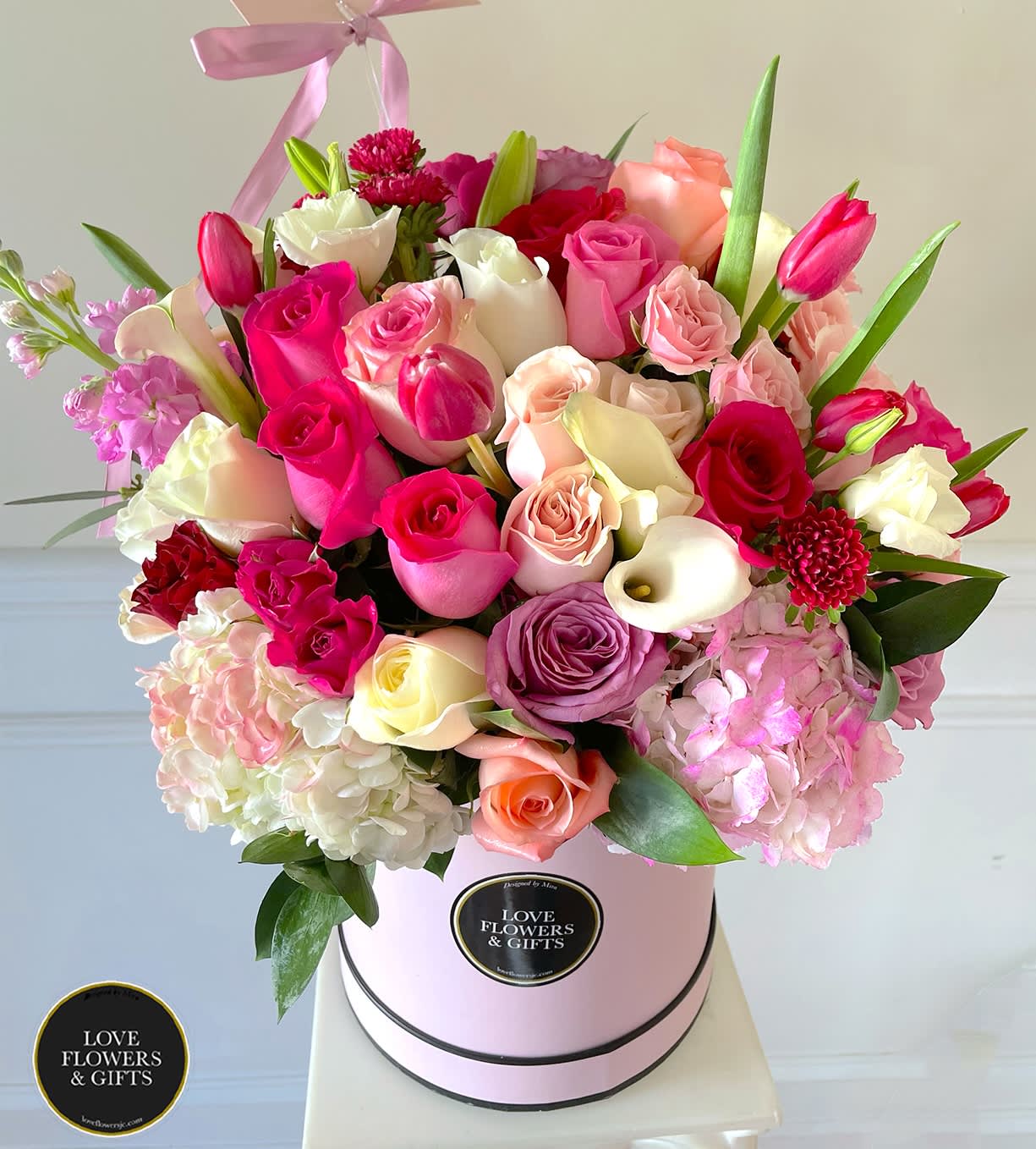 Round hatbox arrangement of mixed pink, white, and peach roses with tulips and calla lilies.