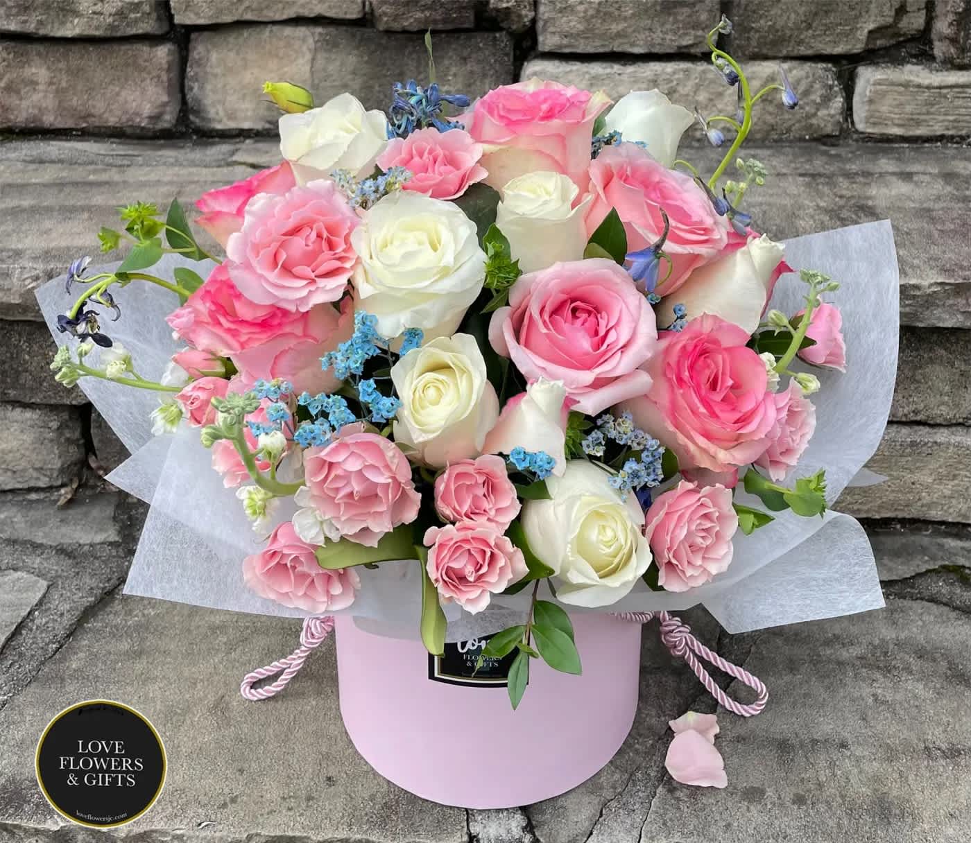 Pink and white rose arrangement in a round pink hatbox with blue filler flowers