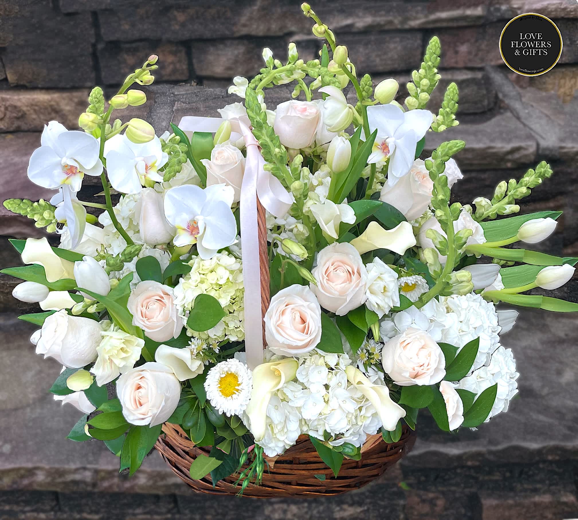 Large basket of white orchids, roses, hydrangeas and calla lilies with soft peach accents.