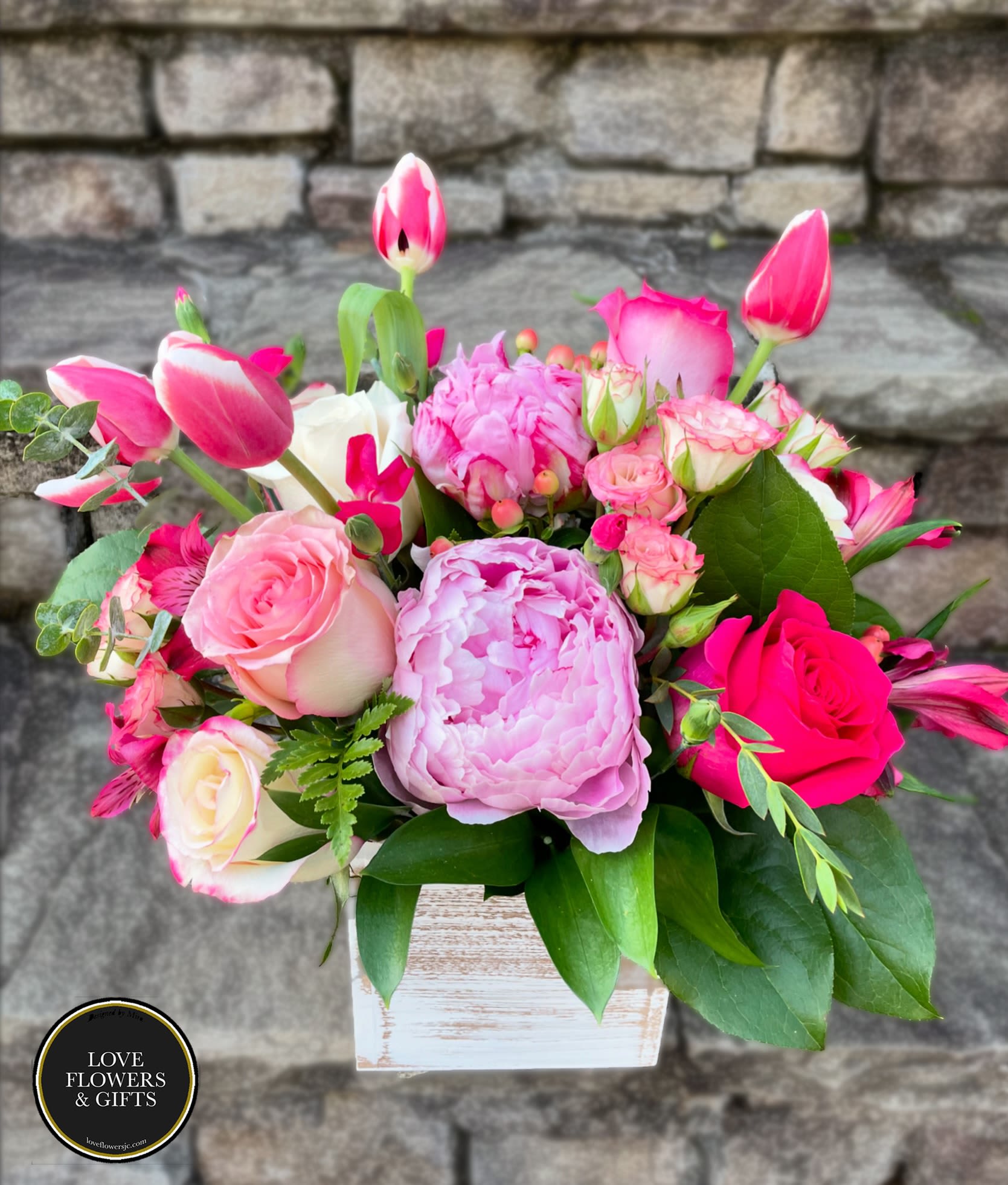 Pink and white peonies, roses, tulips, and other blooms in a whitewashed wood cube vase.