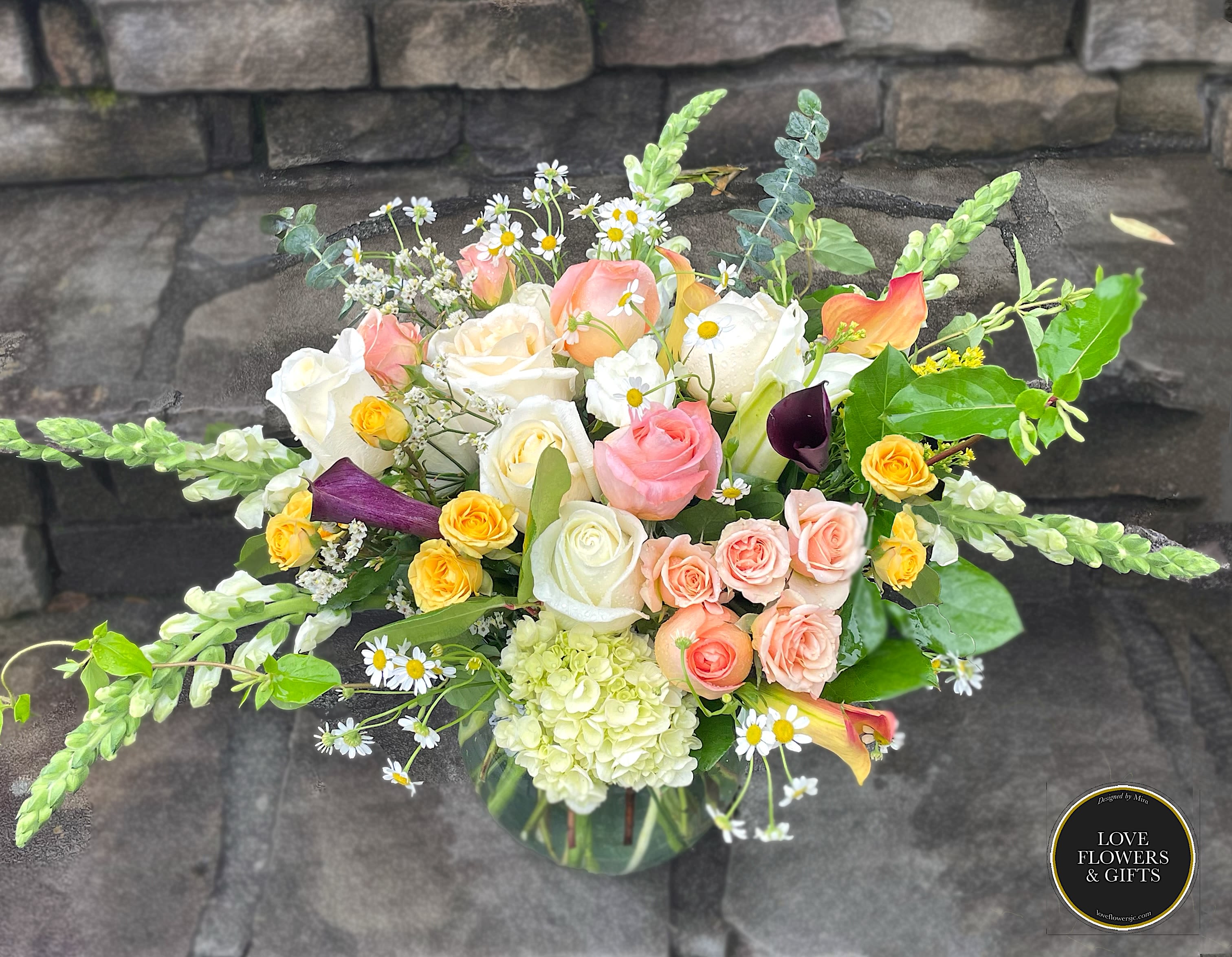 Pastel rose and mixed flower arrangement with snapdragons and calla lilies in a clear glass vase