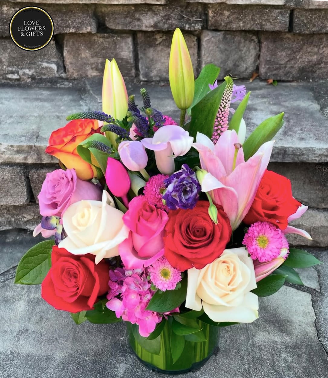 Colorful arrangement of roses, lilies, tulips, and mixed blooms in a clear glass vase