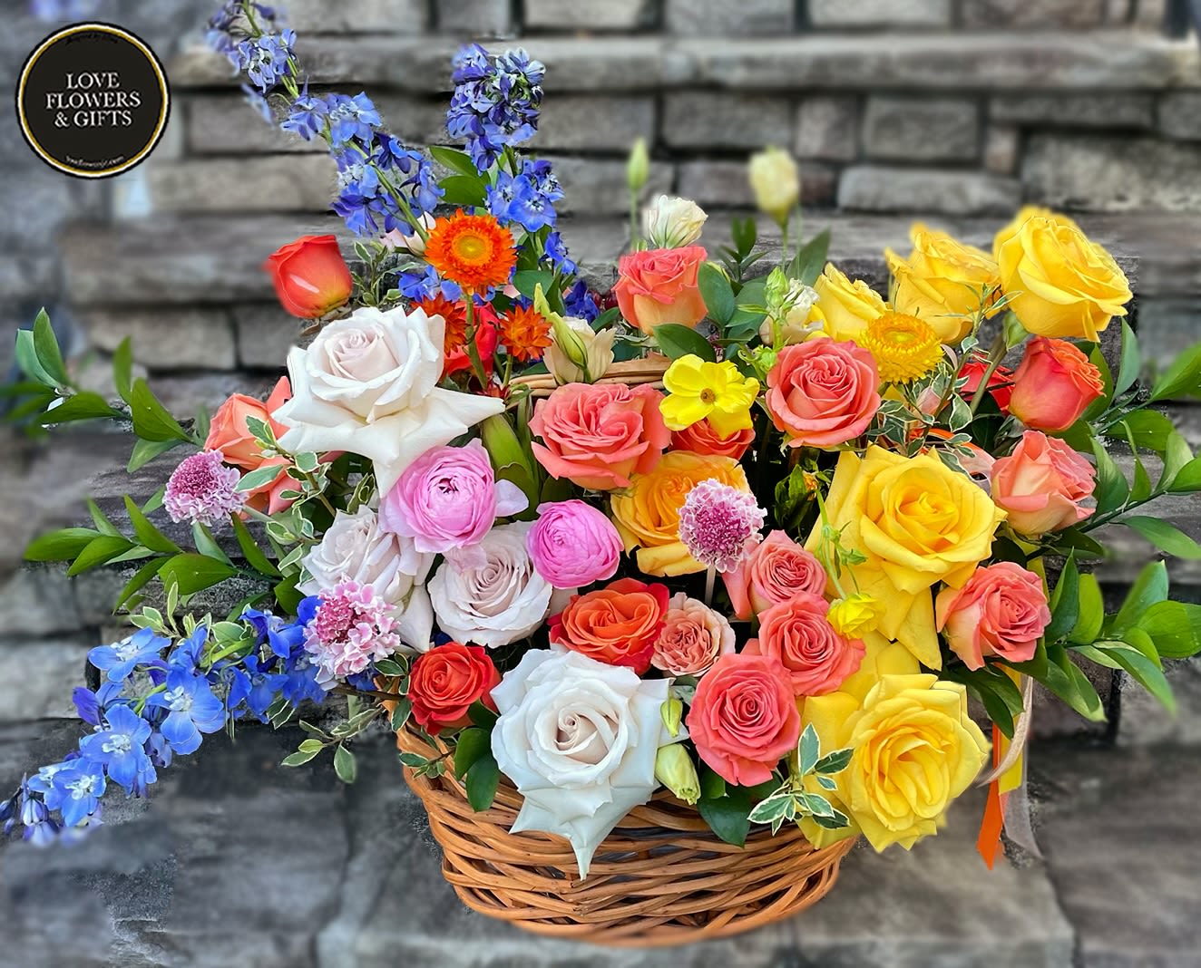 Colorful mixed basket of roses and other blooms in pink, yellow, orange, and blue.