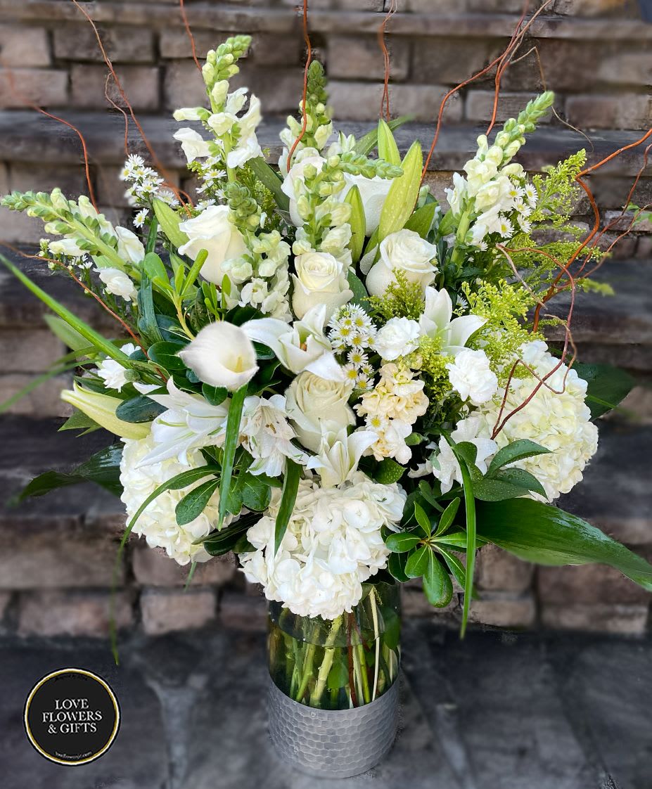 Tall arrangement of white roses, lilies, hydrangeas, and snapdragons in a clear glass vase.