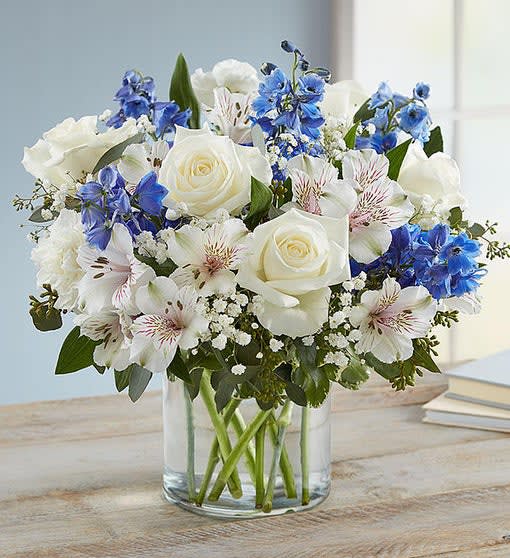 White roses and blue flowers arranged in a clear glass vase