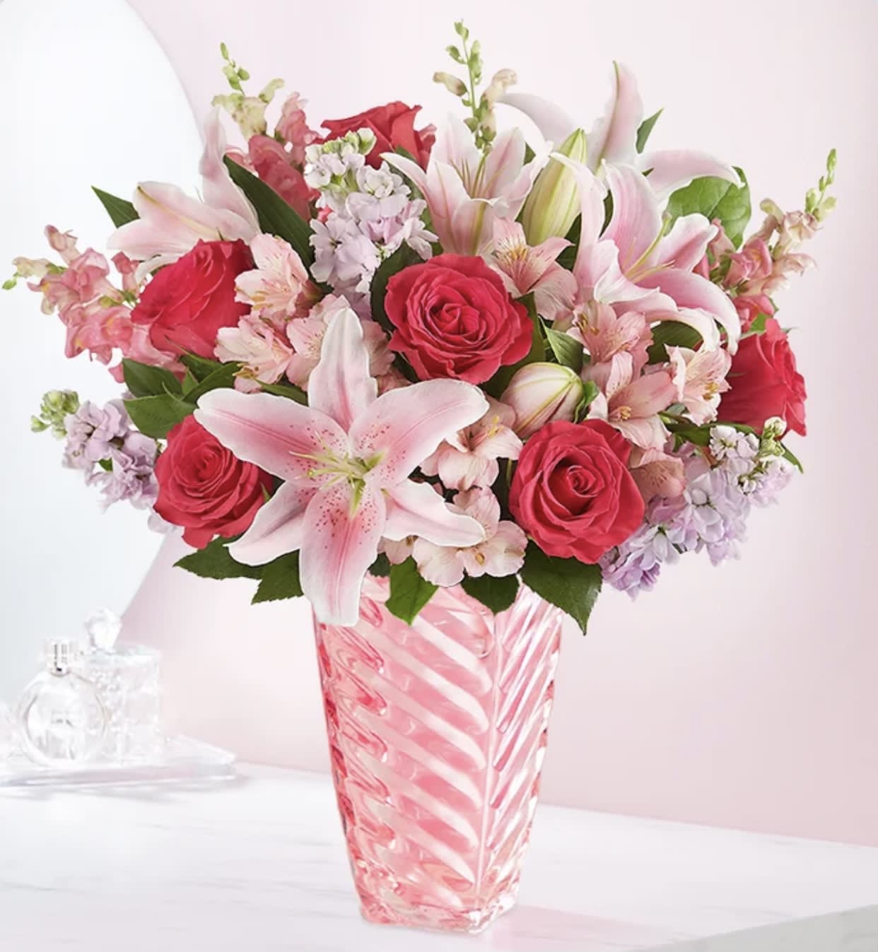 Pink lilies and red roses arranged in a striped glass vase