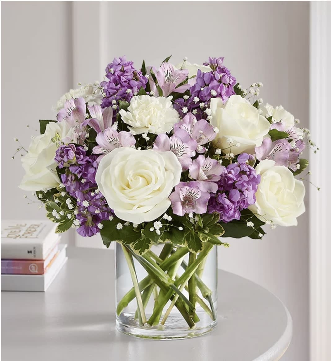 White roses and purple flowers arranged in a clear glass vase