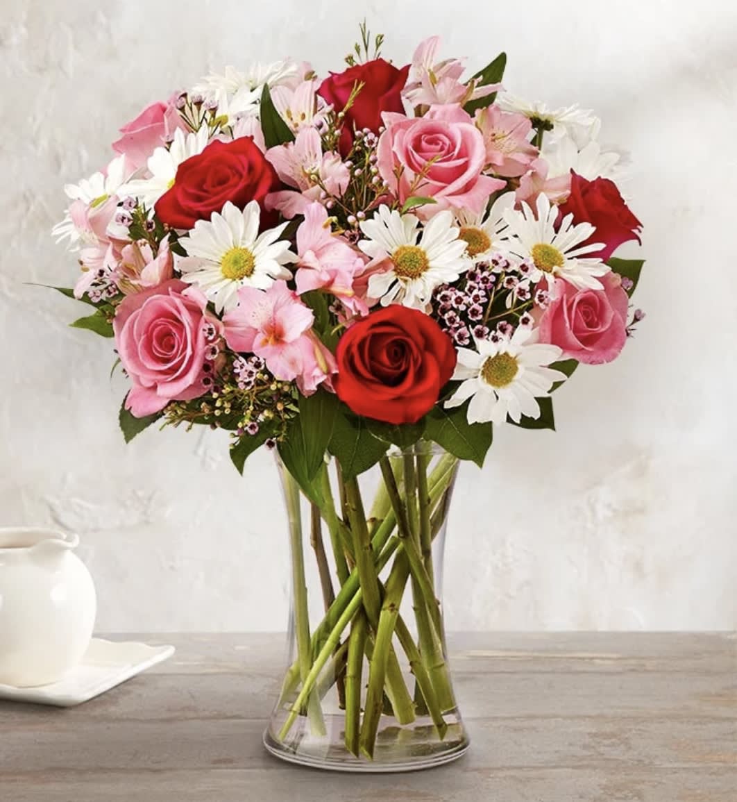 Bouquet of red and pink roses with white daisies in a clear glass vase