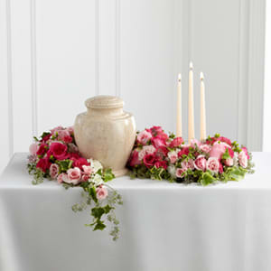 Pink rose floral arrangement around a beige urn with three taper candles