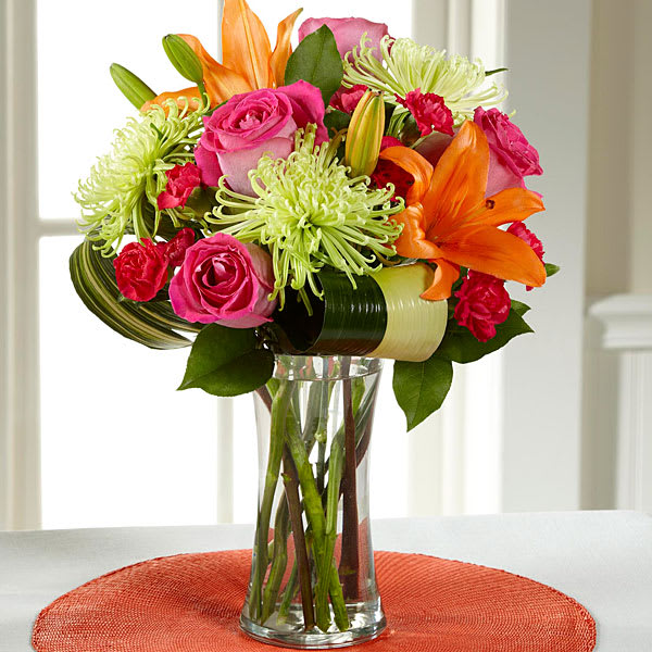 Bright mixed bouquet of roses, lilies, and green spider mums in a glass vase