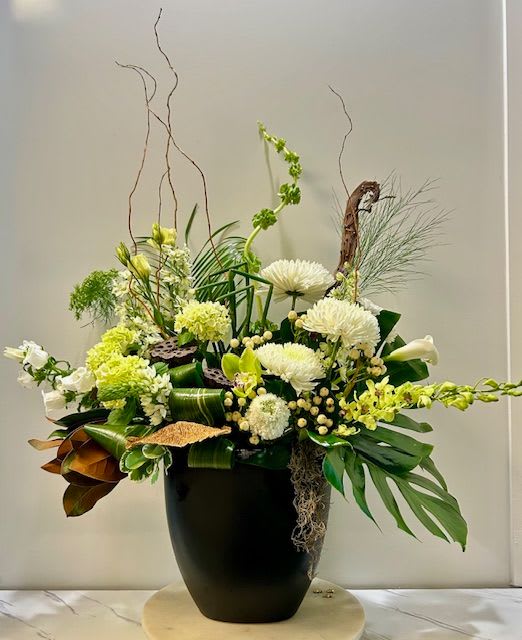 Tall floral arrangement with white and green blooms in a black vase