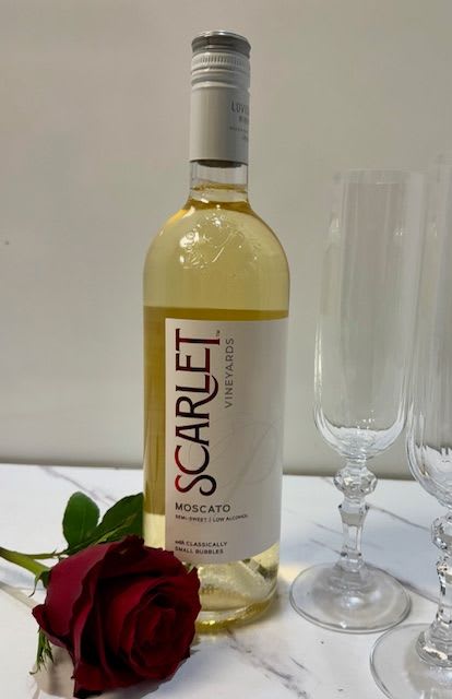 Bottle of white wine beside a red rose and two champagne flutes
