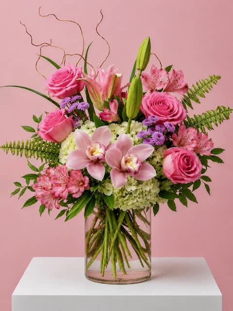 Pink roses, lilies, and orchids arranged in a clear glass vase