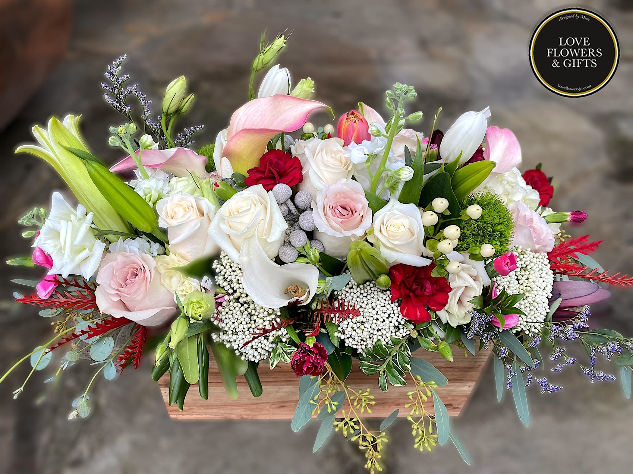 Low wooden box arrangement with white and pink roses, calla lilies, lilies, and red accent flowers