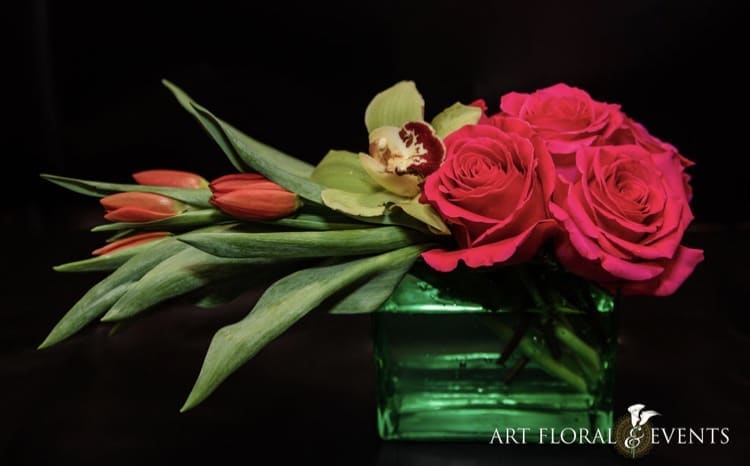 Pink roses and tulips arranged in a green glass vase