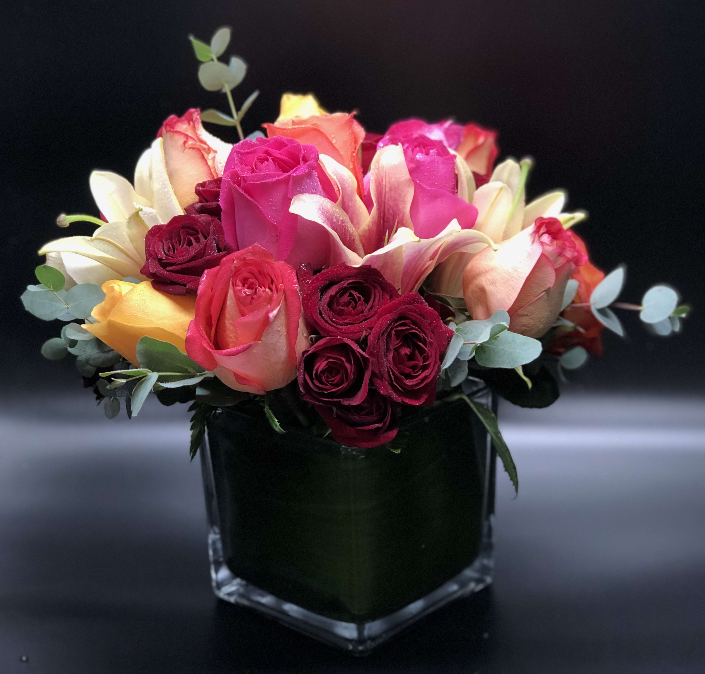 Bouquet of pink, red, and peach roses in a square glass vase