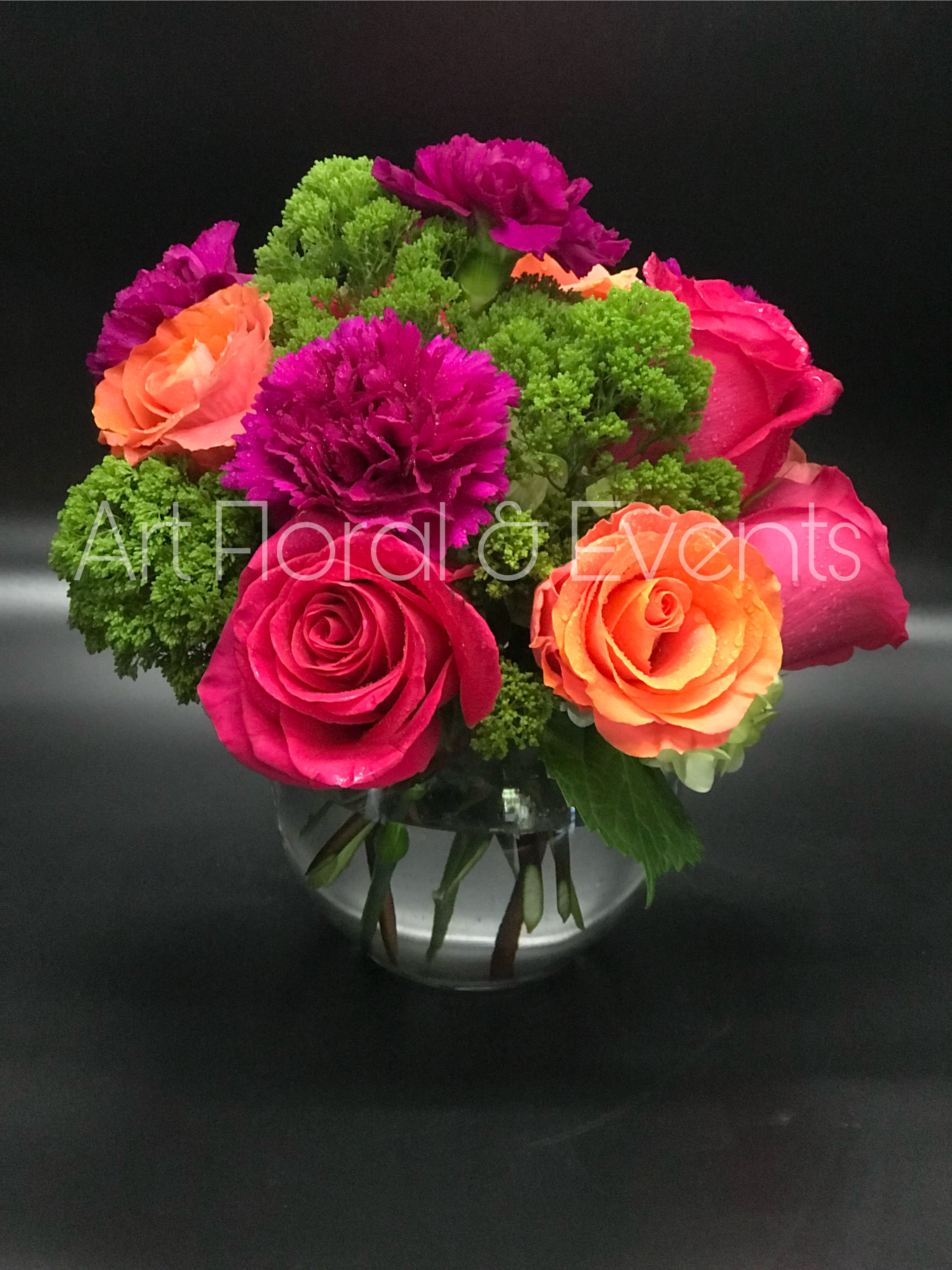 Bright pink and orange roses with purple carnations in a glass vase