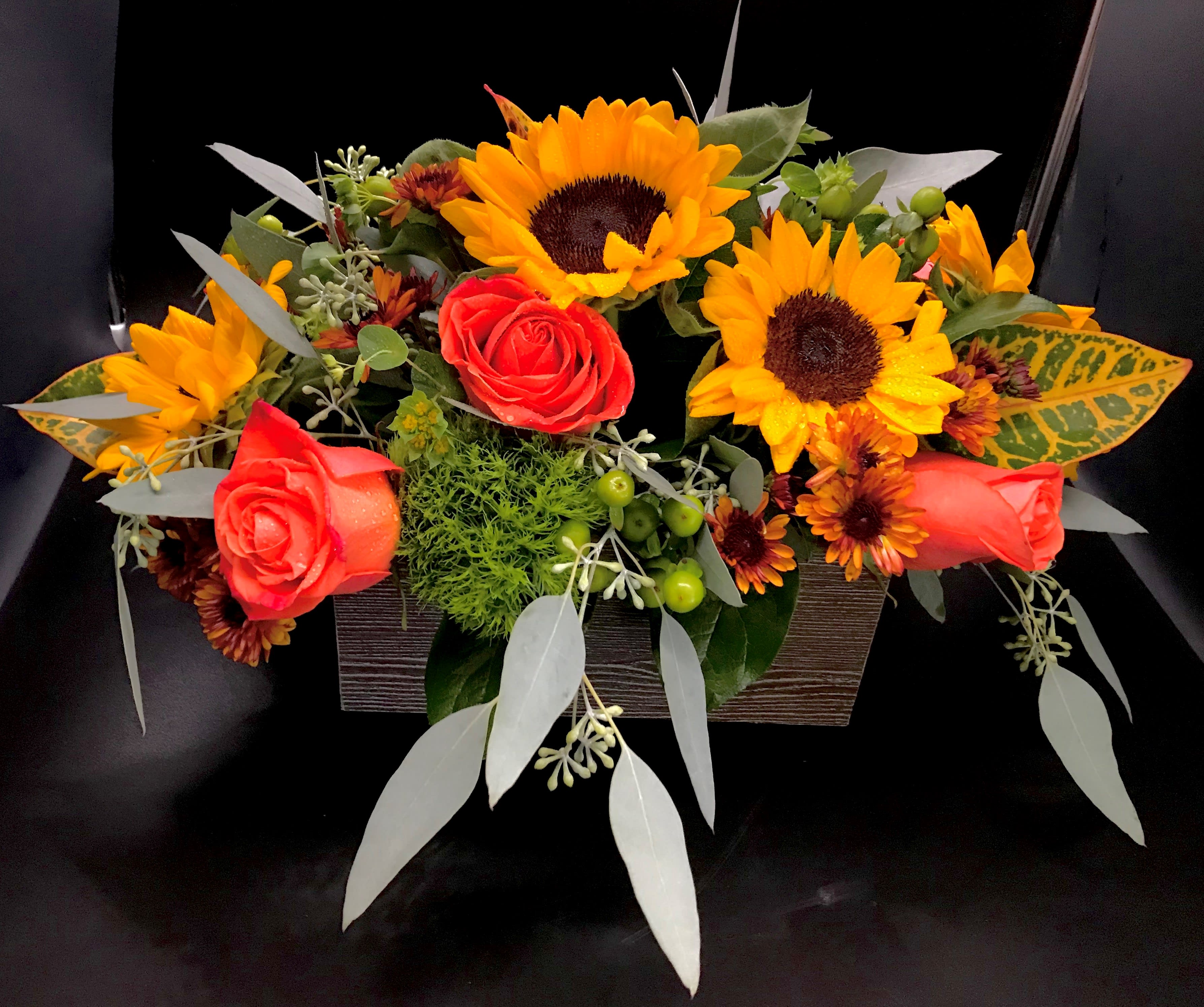 Arrangement of red roses and yellow sunflowers in a rectangular container