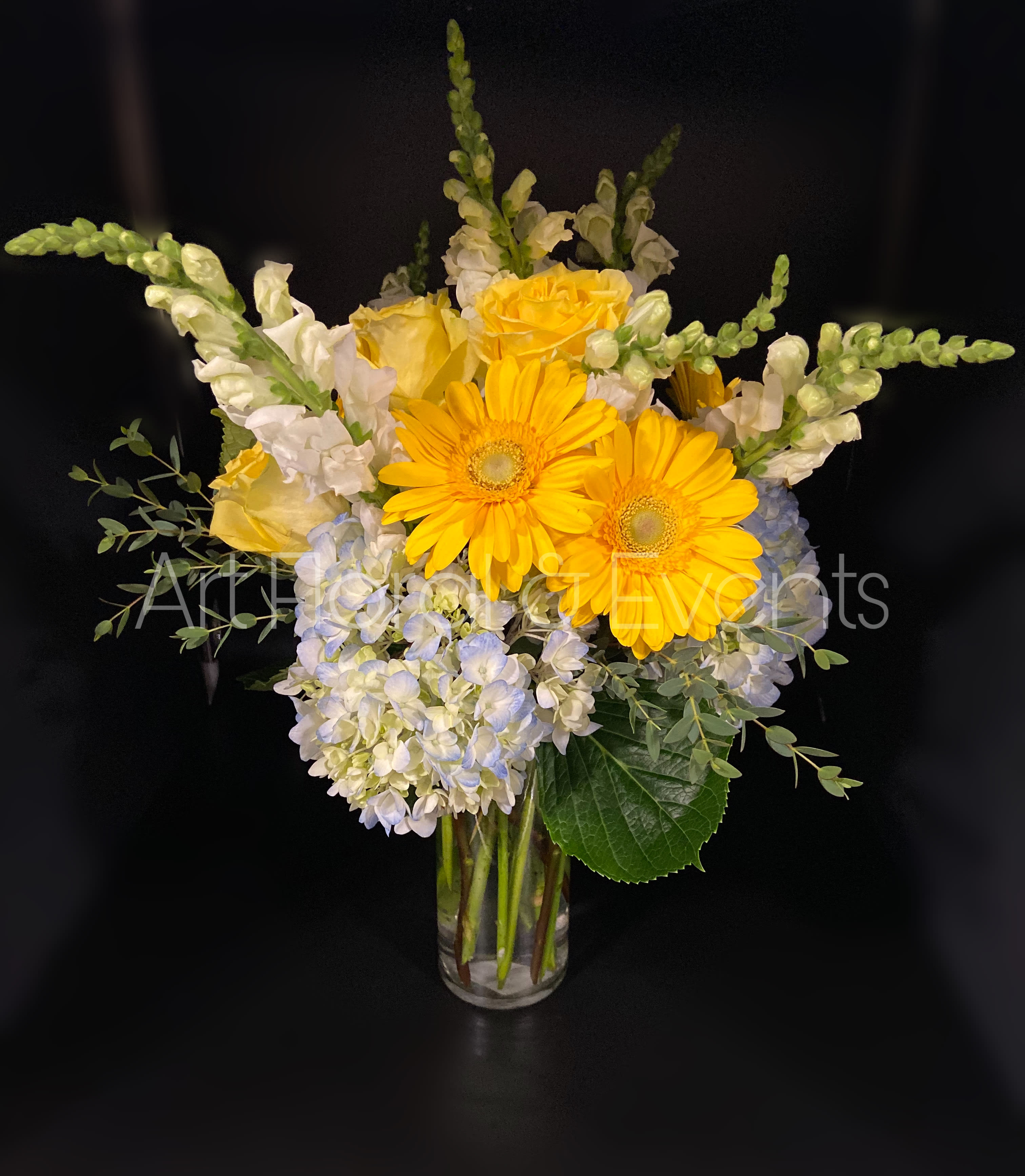 Yellow gerbera daisies and white flowers in a clear glass vase