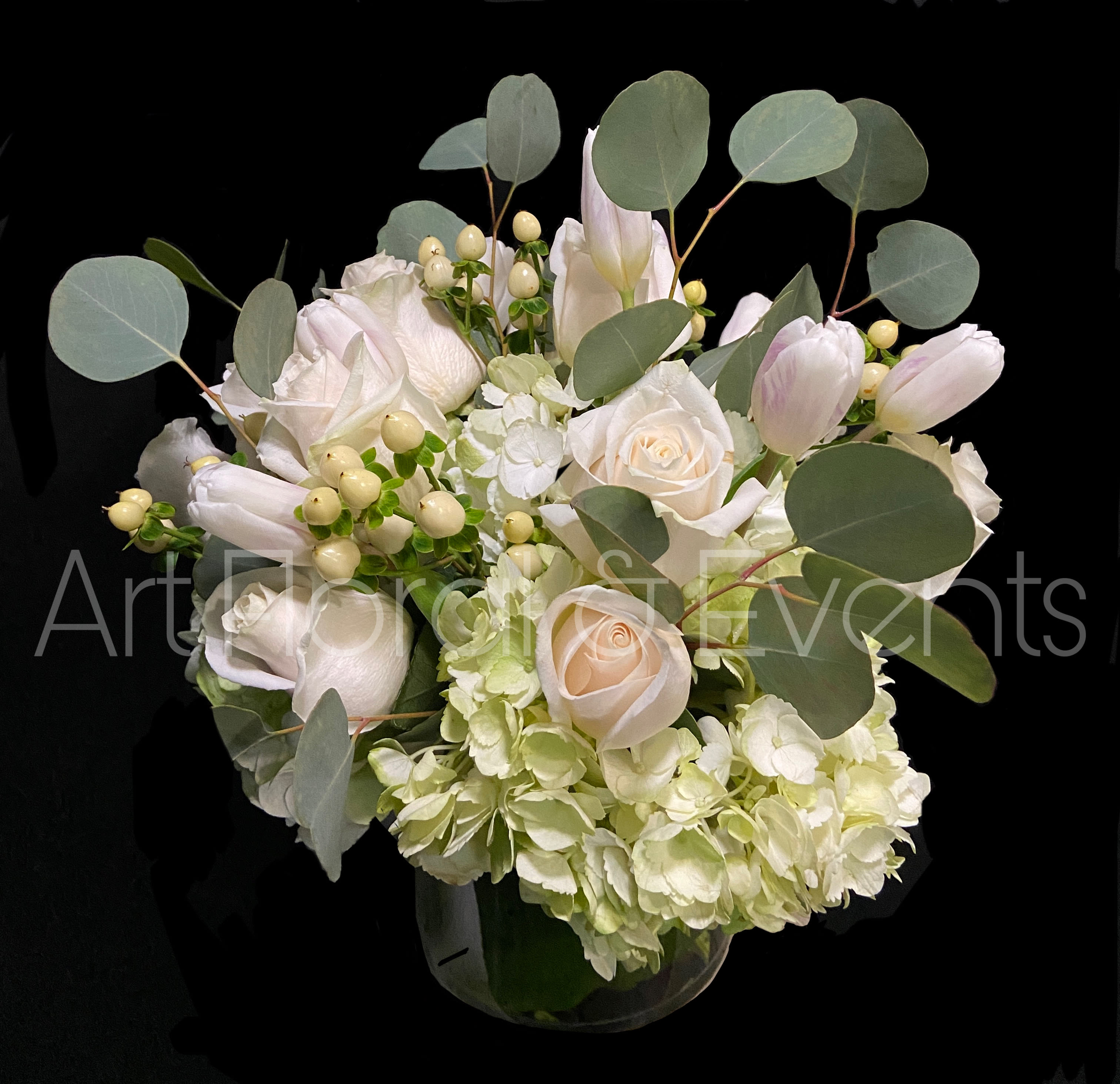 White roses and pale tulips in a glass vase with round eucalyptus leaves